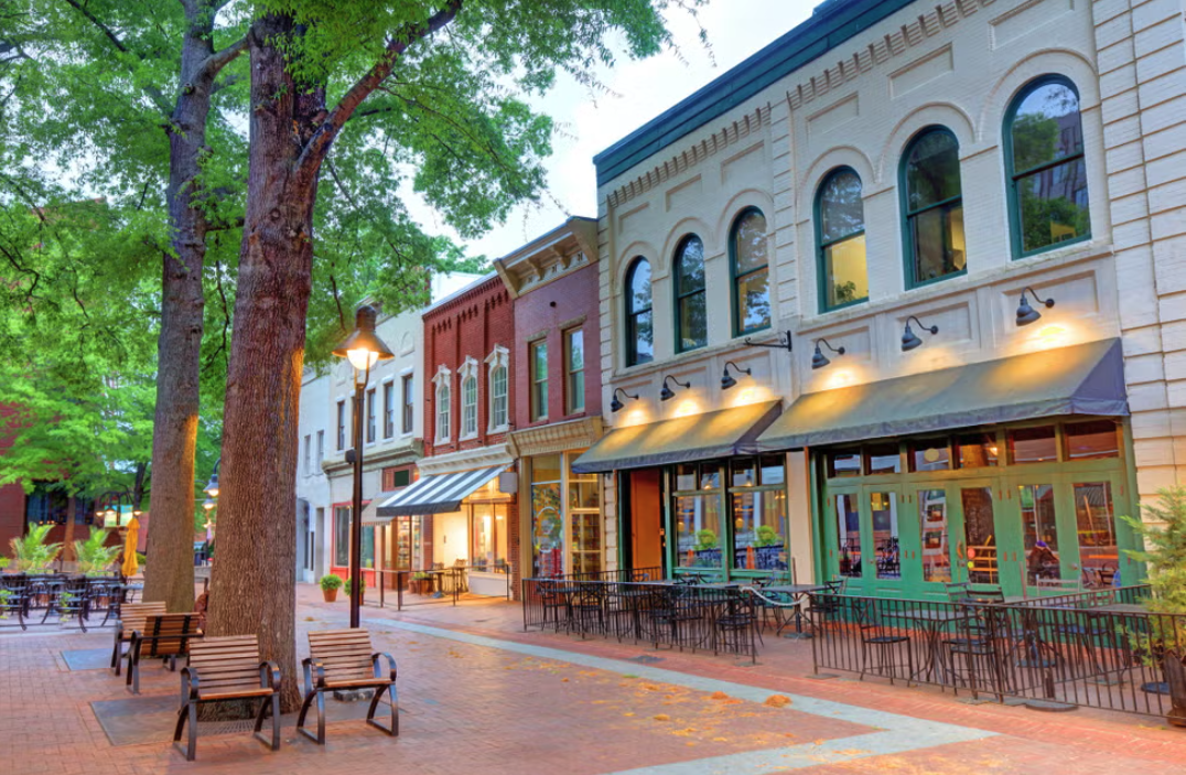 Empty outdoor shopping or dining area with benches, trees, storefronts, and street lamps in Charlottesville, Virginia.