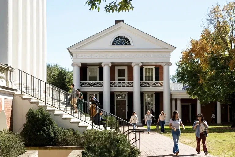 Students walking on University of Virginia campus stairs and sidewalk in front of a historic building with white columns and brick facade.