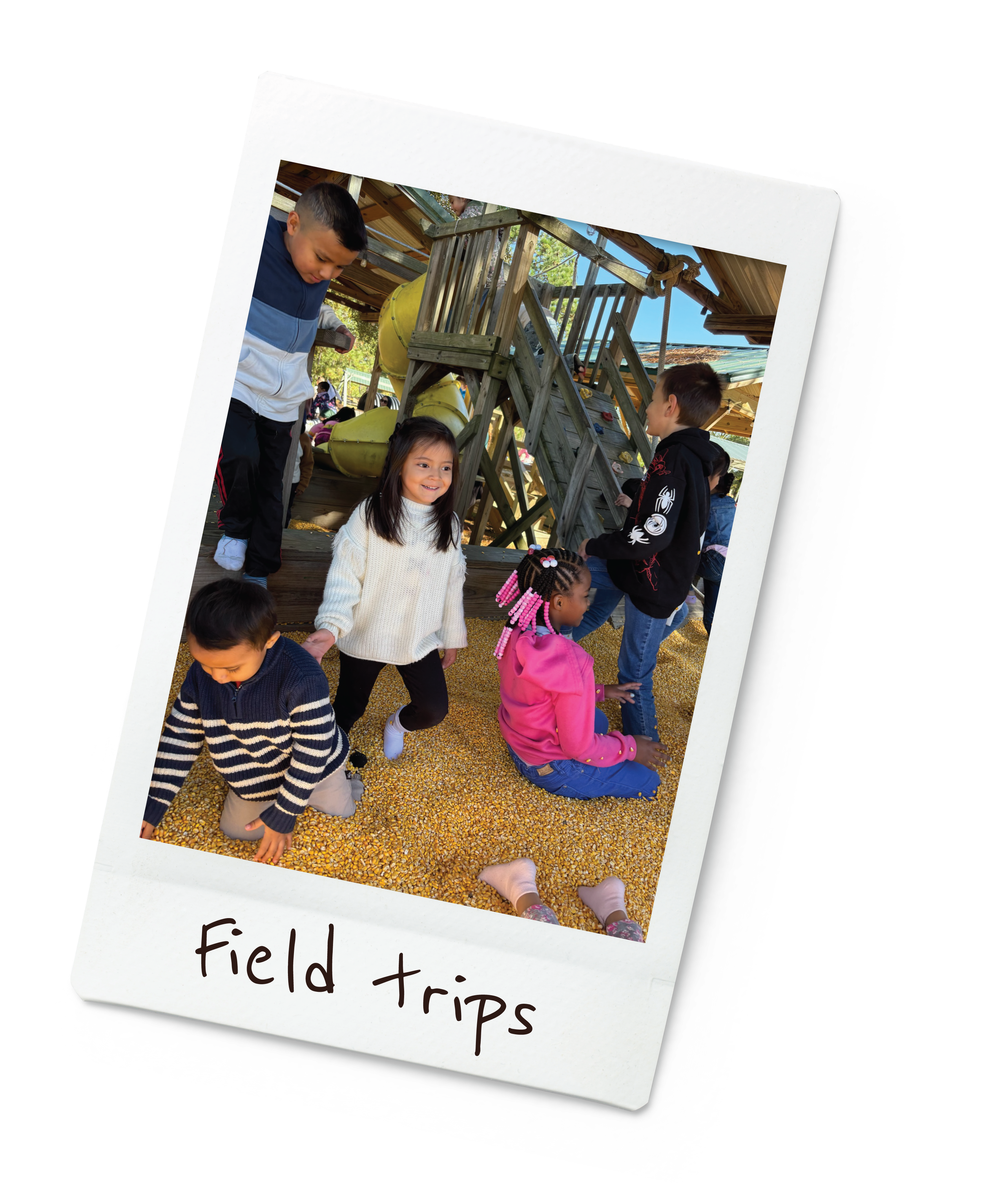 Children playing and exploring in a gravel-filled playground with a wooden play structure, slide, and rope ladder during a field trip.