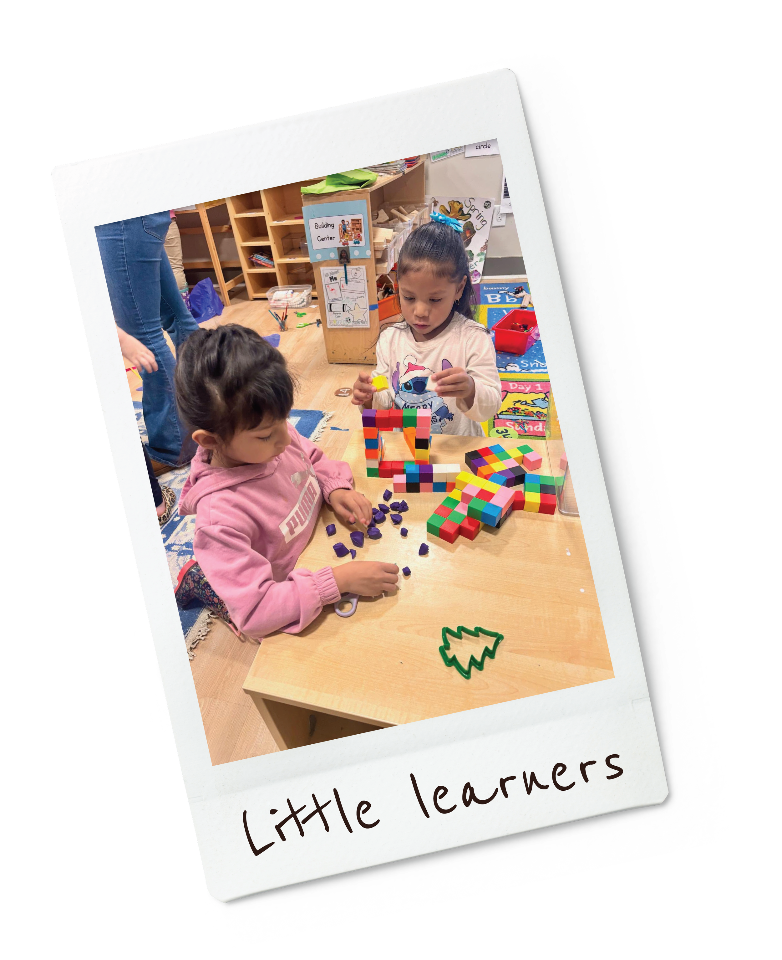 Two young girls playing with colorful toys and building blocks at a table in a classroom labeled "Little learners."