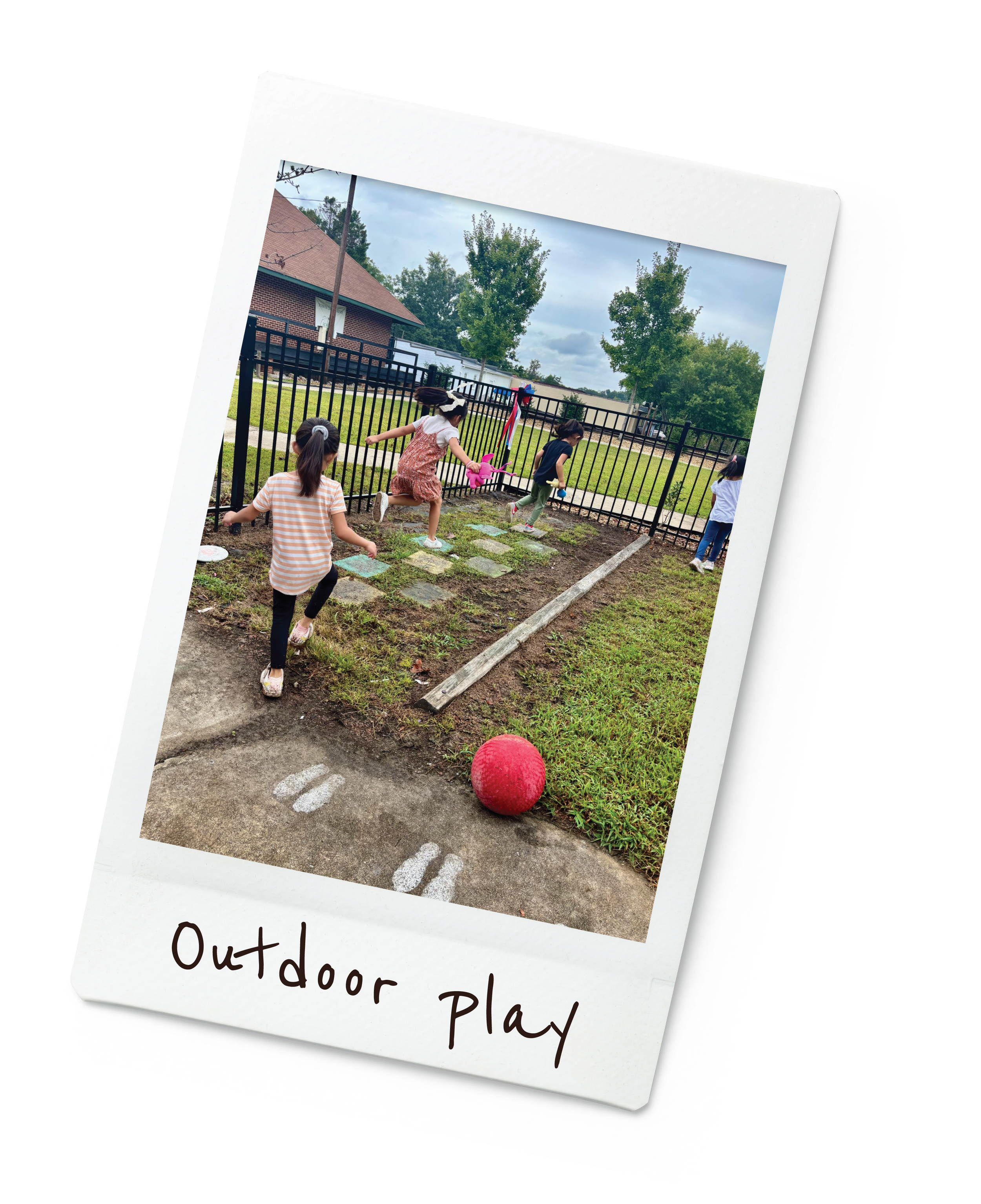 Children playing outside near a black fence with grass and trees in background.