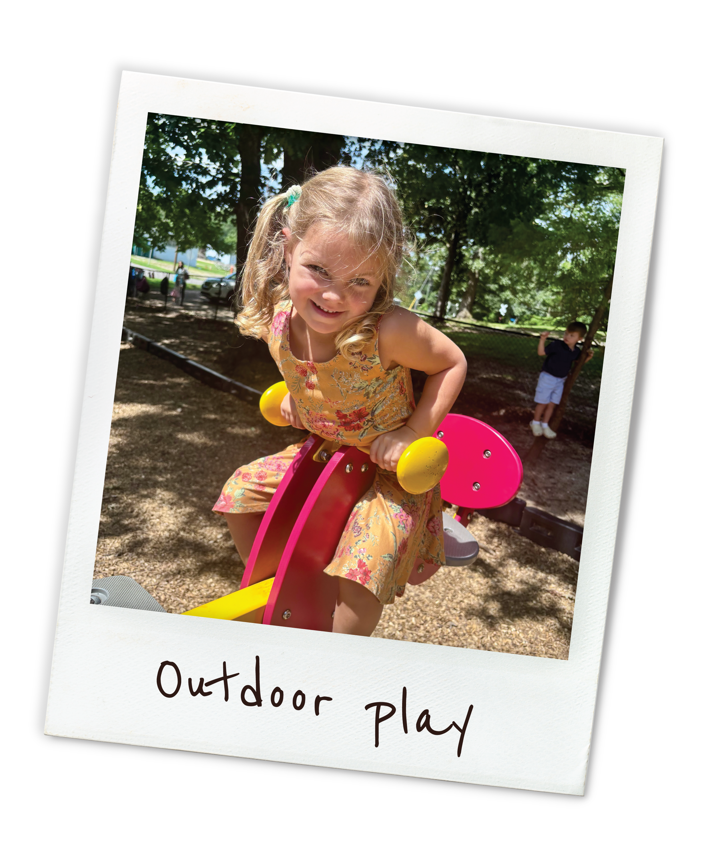 A young girl smiling while sitting on a playground ride in a park, with trees and a boy in the background, under a sunny sky.