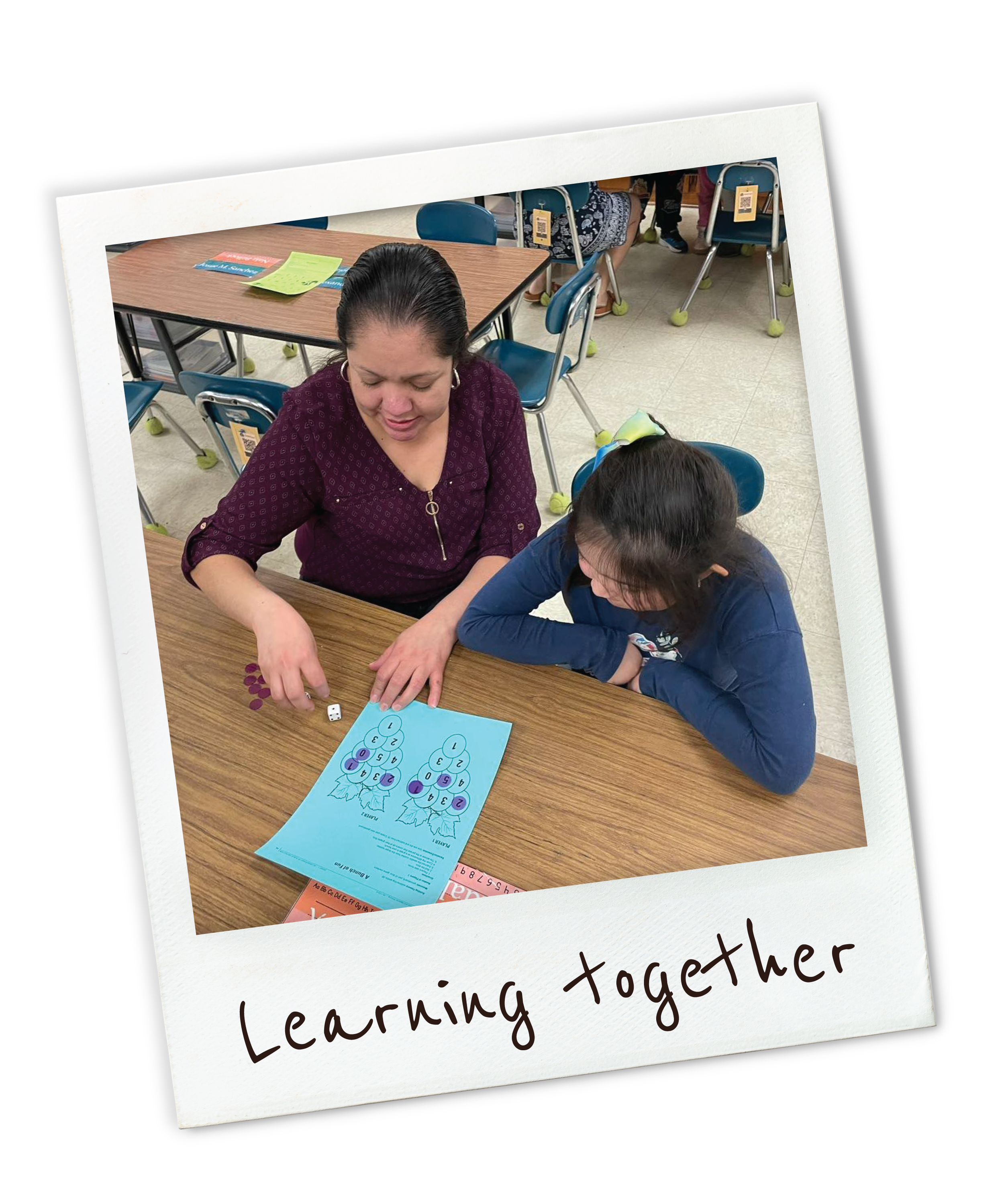 Adult and child playing a math game with dice and a worksheet on a classroom table.