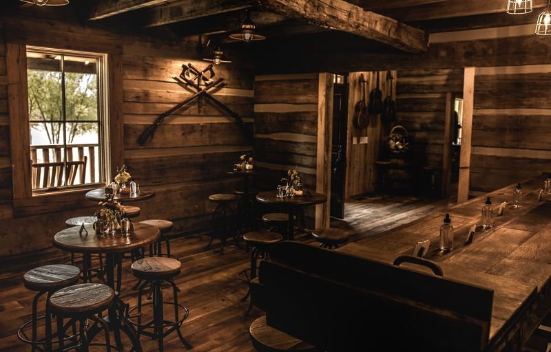 Interior of a rustic wooden restaurant or cafe with round tables, bar stools, and guitars hanging on the wall.