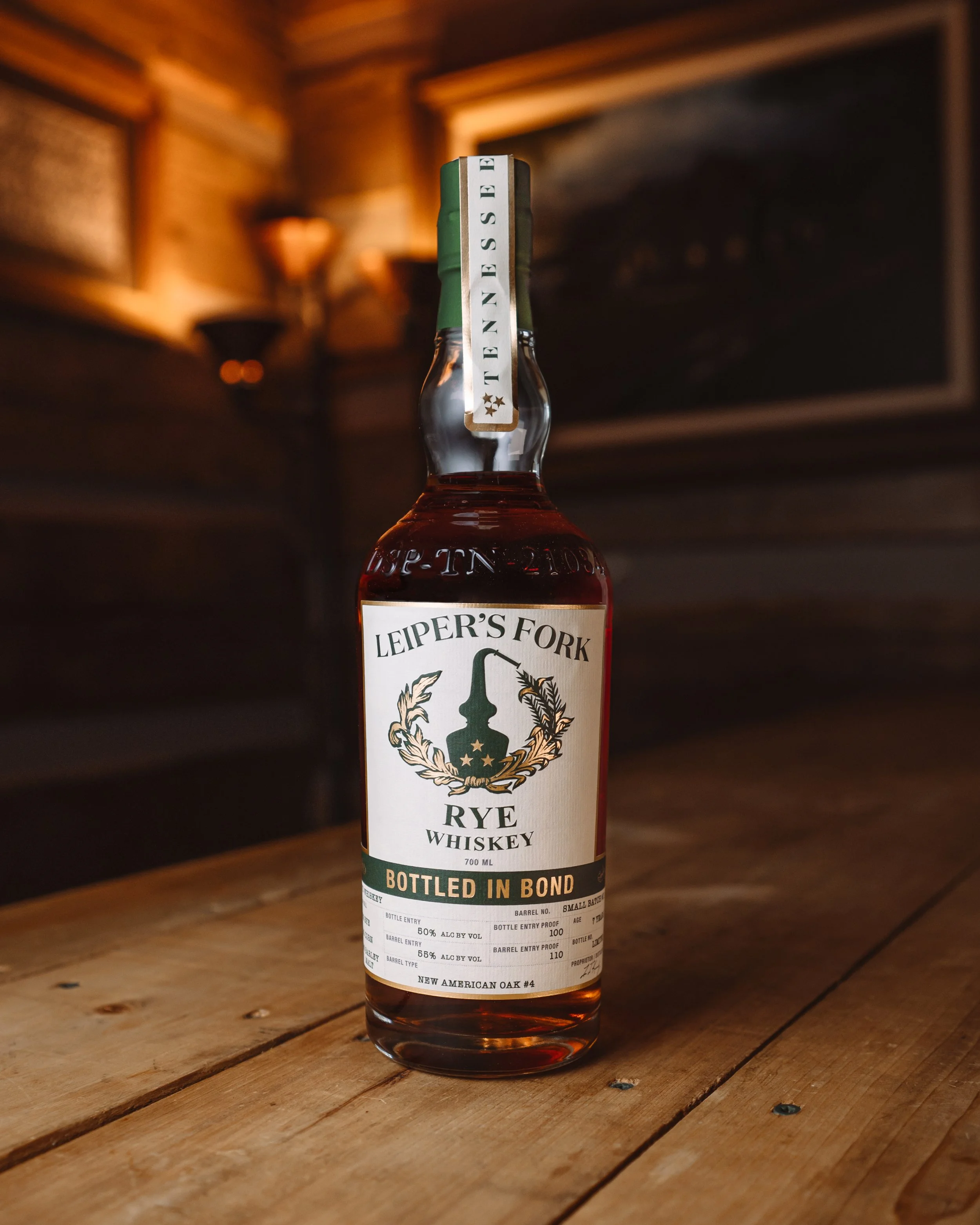 A bottle of Leiper's Fork Rye Whiskey on a wooden table in a rustic setting.