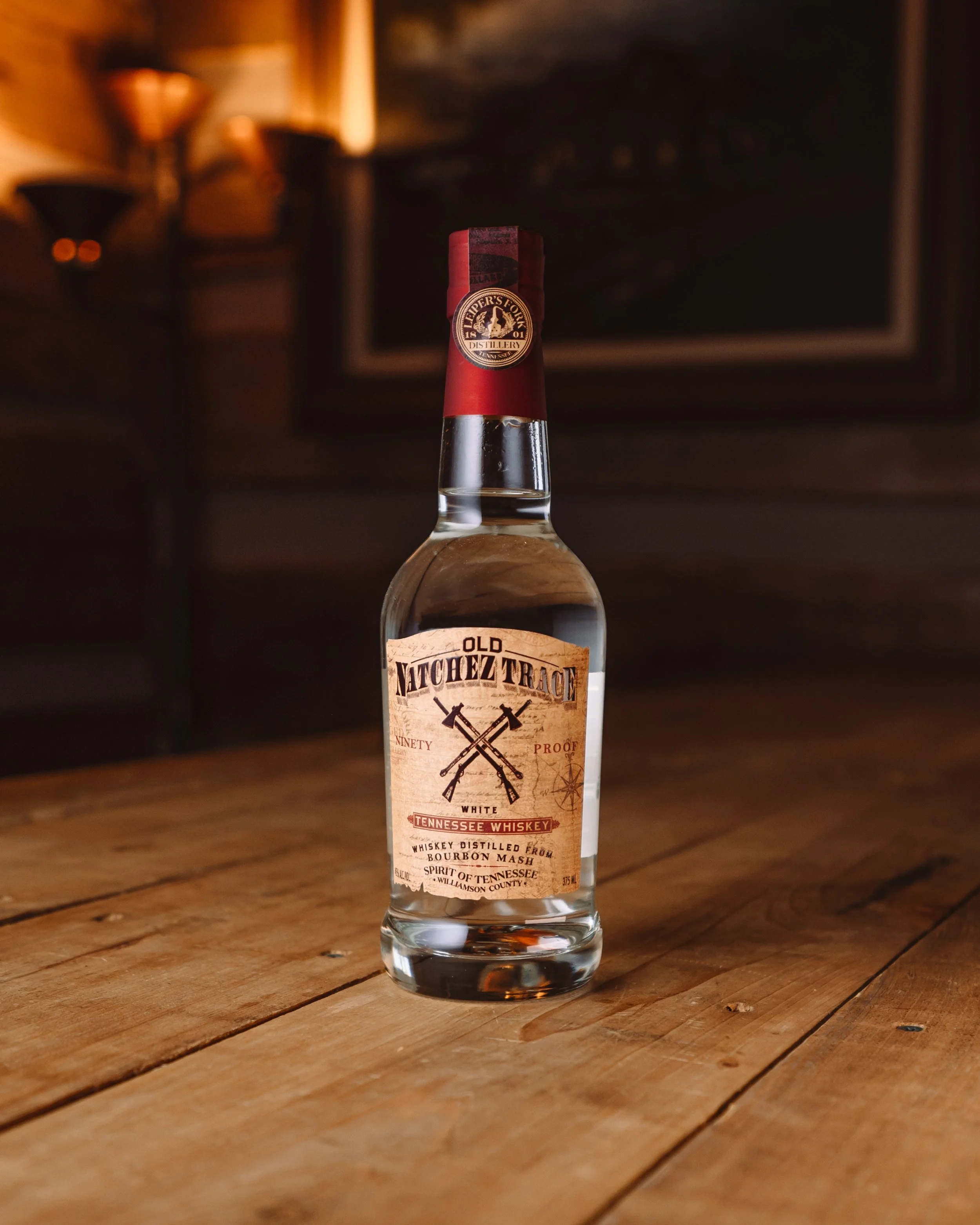 A bottle of Old Natchez Trace Tennessee Whiskey on a wooden table in a dimly lit room.