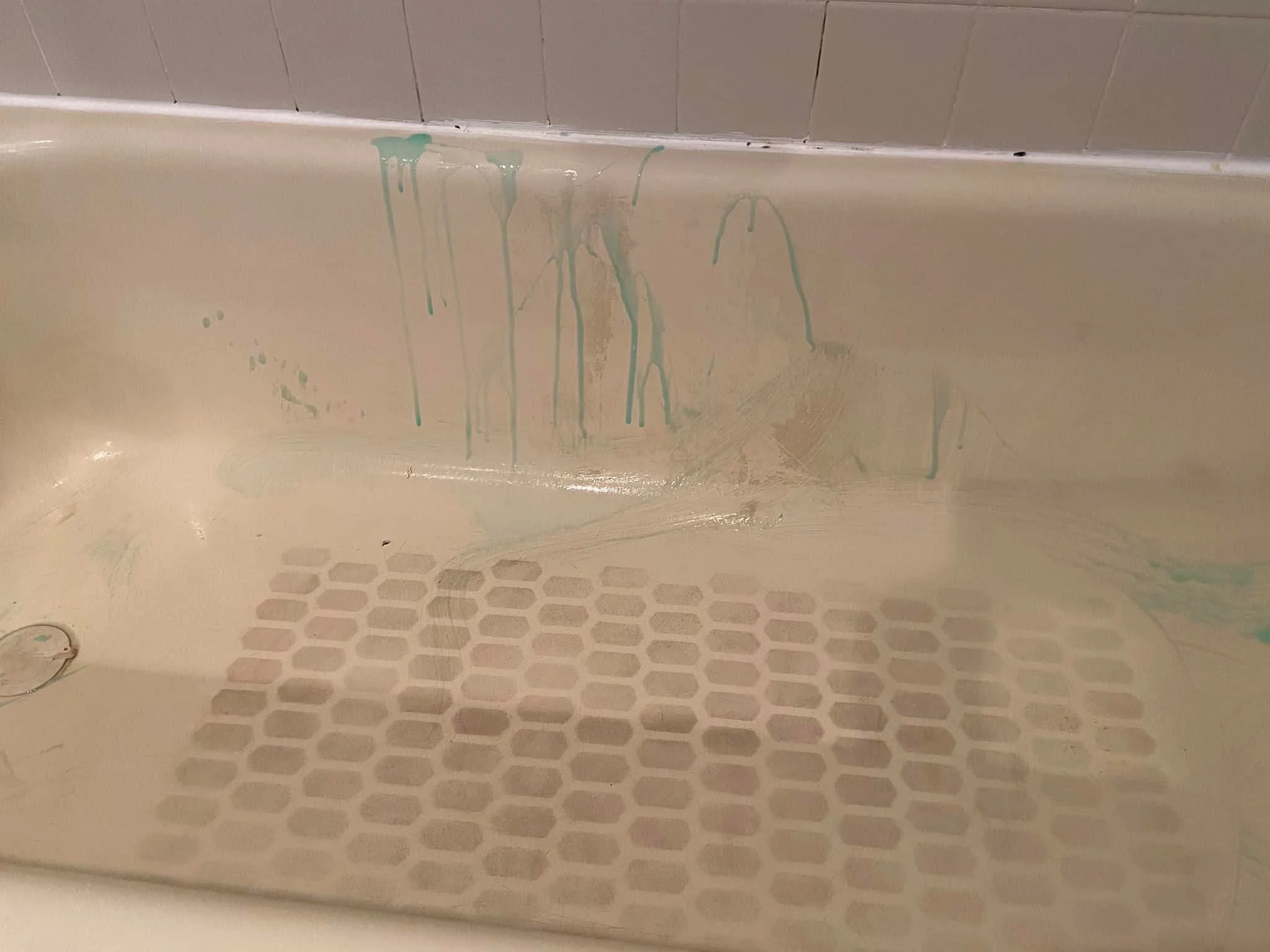 A beige bathtub with teal paint drips on the side, and a white tiled wall at the top of the image.