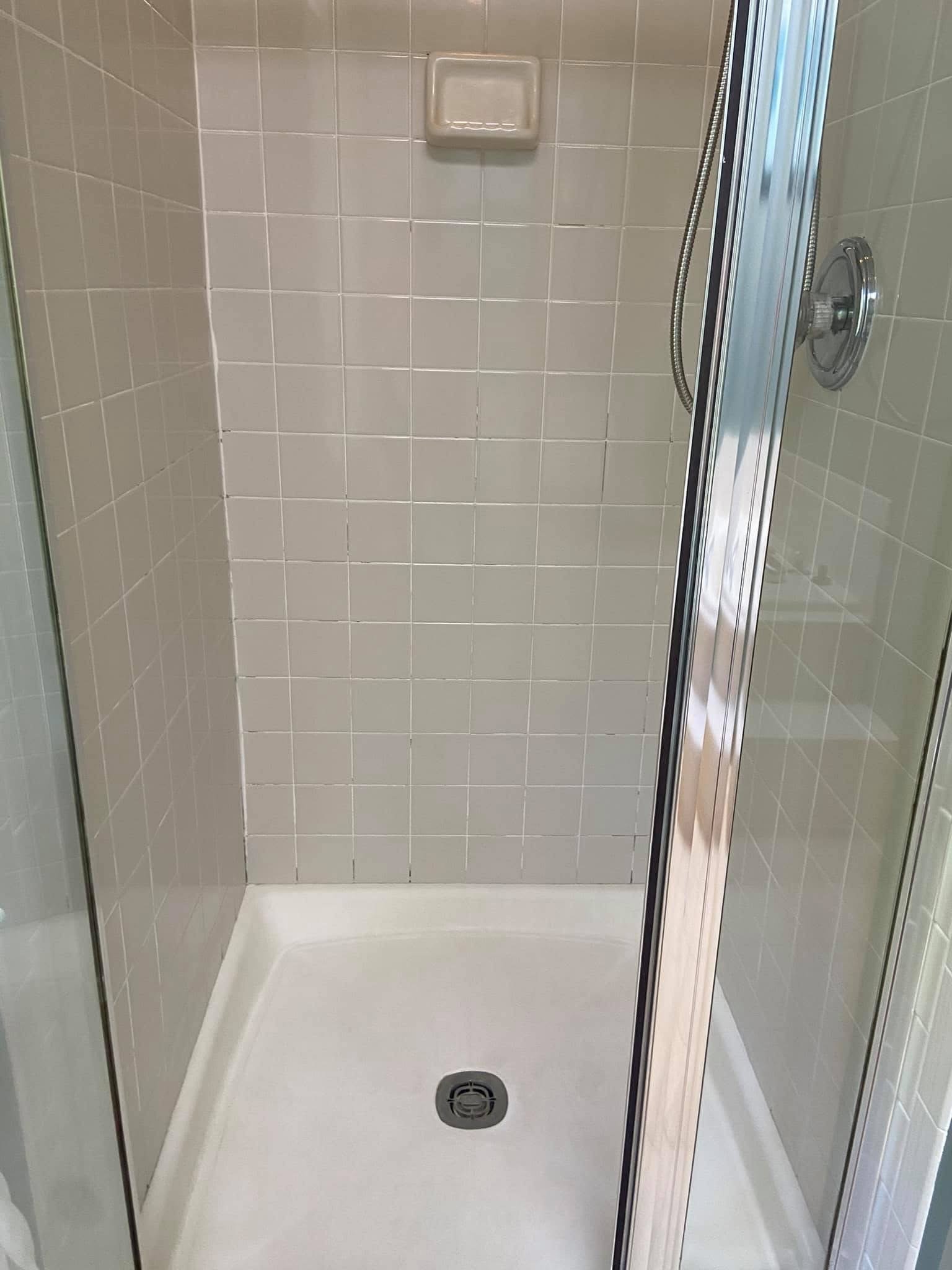 Empty shower with beige tiled walls, a soap dish, and a central drain on the white shower floor.