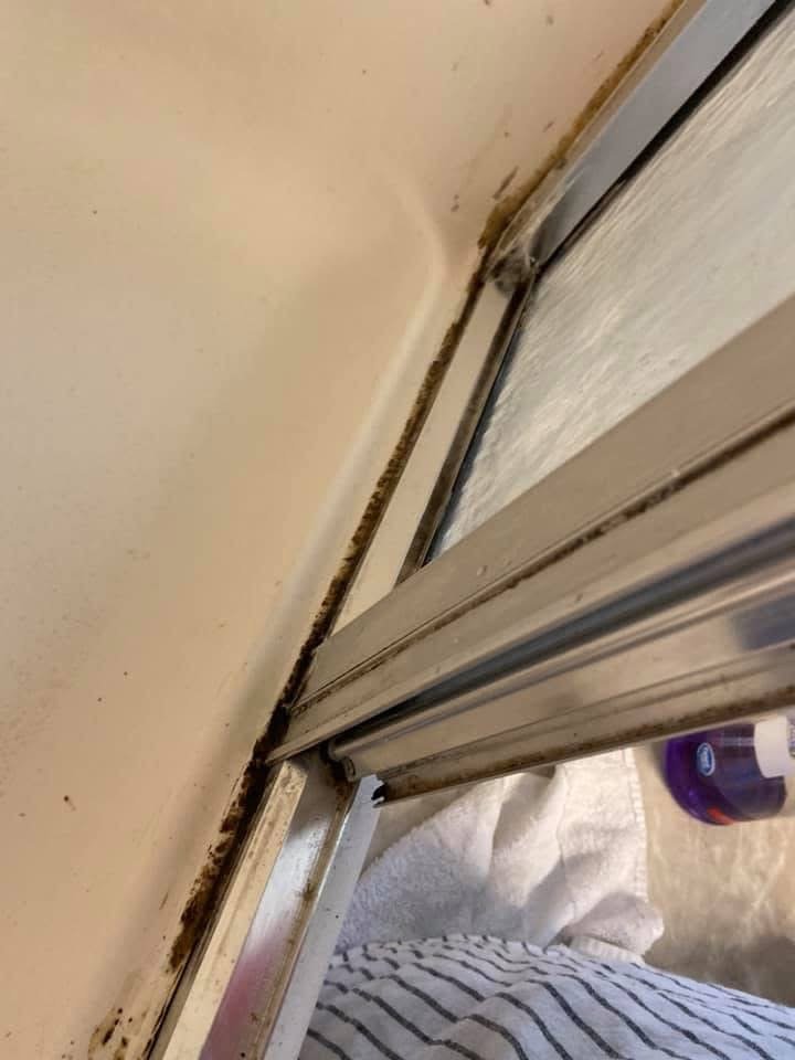 Close-up photo of a sliding door track with visible dirt and grime, with a towel and a bottle nearby.