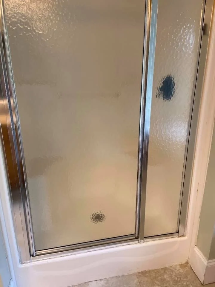 Frosted glass shower door with metal frame and a small hole at the bottom, and another hole on the right side.