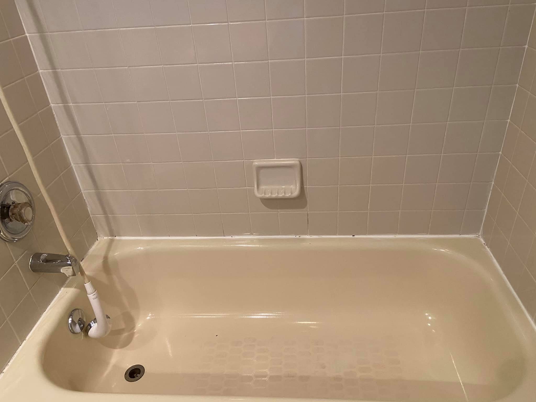 A shower with beige tiles, a soap dish, and a handheld showerhead.