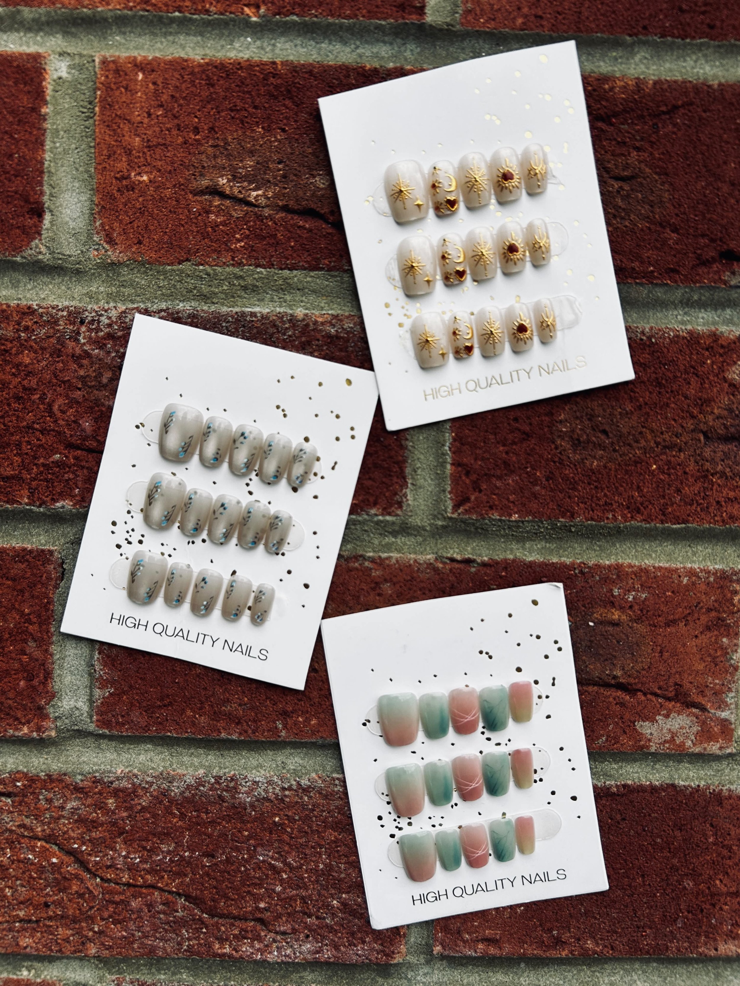 Several sets of decorative high-quality nail polish stickers with various designs, including celestial and gemstone motifs, placed on white backing cards, on a red brick background.