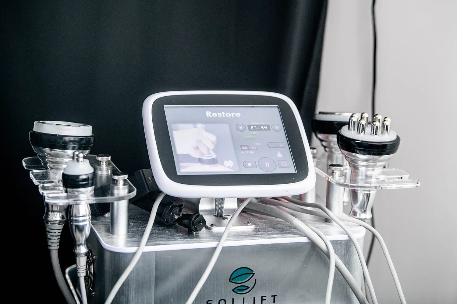 A close-up of a professional body sculpting and skin tightening machine with a digital display showing "Restore" and a timer set to 27:34.