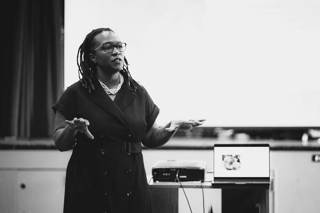 Dr. Clarece Weinraub speaking at a podium during a presentation – Founder of VibeCheckCo sharing insights on culture, feedback, and program evaluation for schools and nonprofits in Los Angeles.