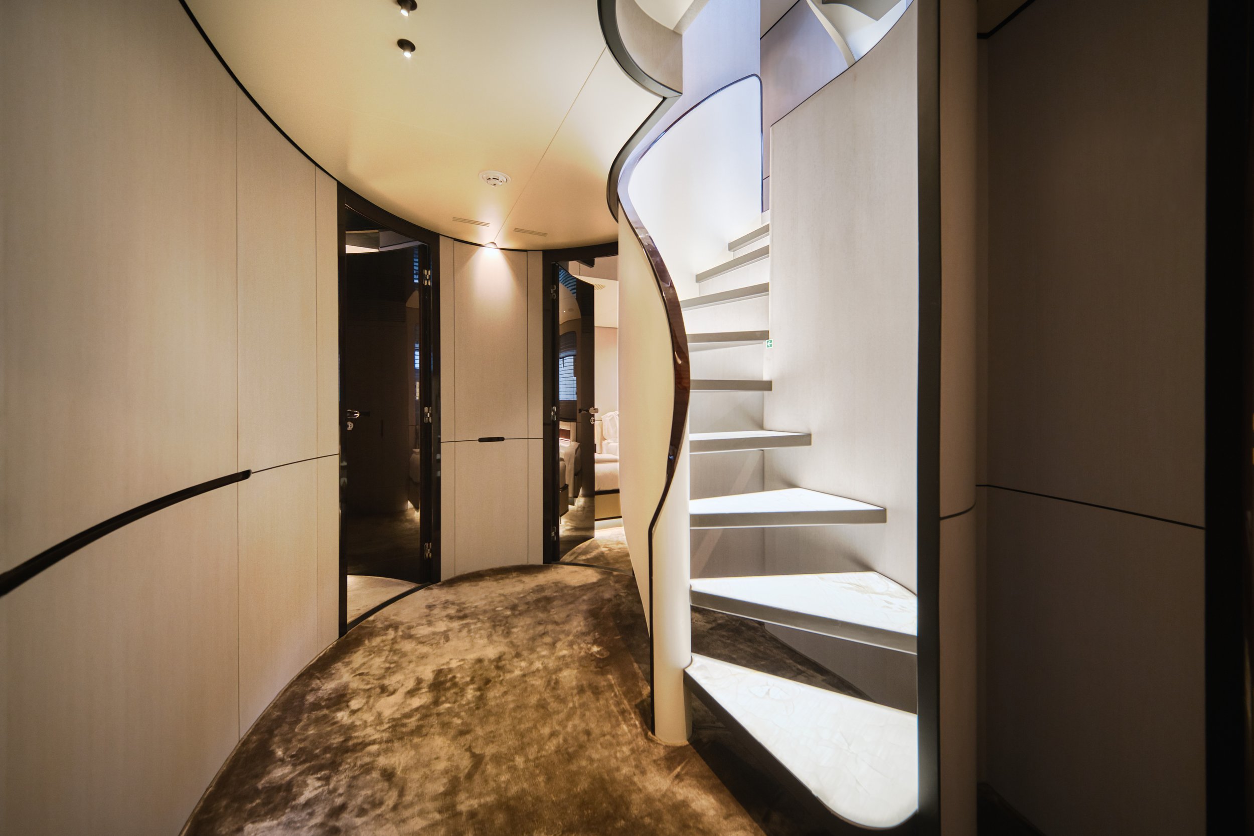 Vue intérieure d'un escalier en colimaçon blanc avec rambarde en bois, entouré de murs en panneaux clairs, dans un espace moderne et élégant.