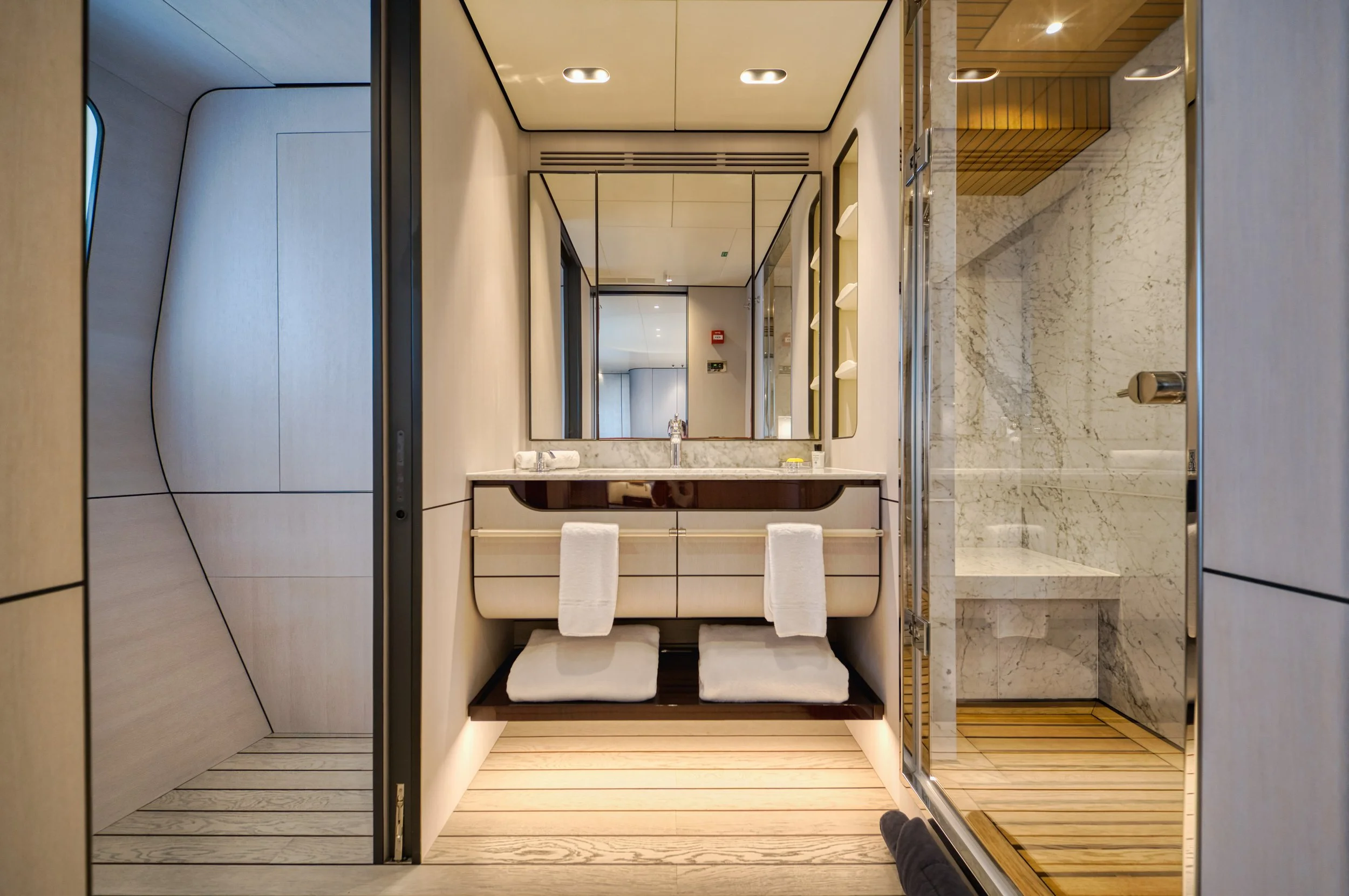 Salle de bain moderne avec lavabo, miroir, serviettes, et douche en coin avec murs en marbre et revêtement de sol en bois.