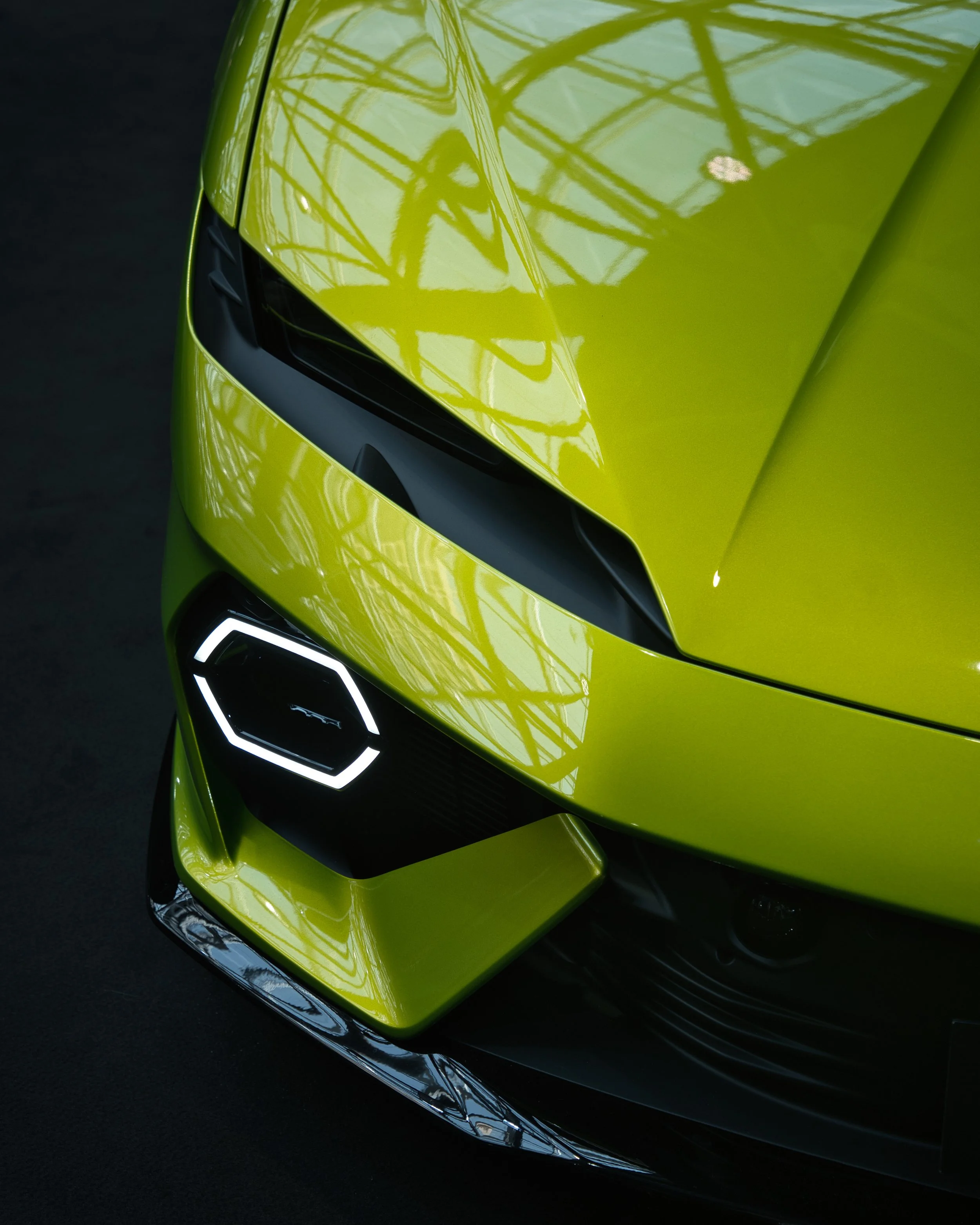 Vue partielle d'une voiture sportive verte, mettant en valeur la calandre, le phares et la peinture brillante avec des reflets.