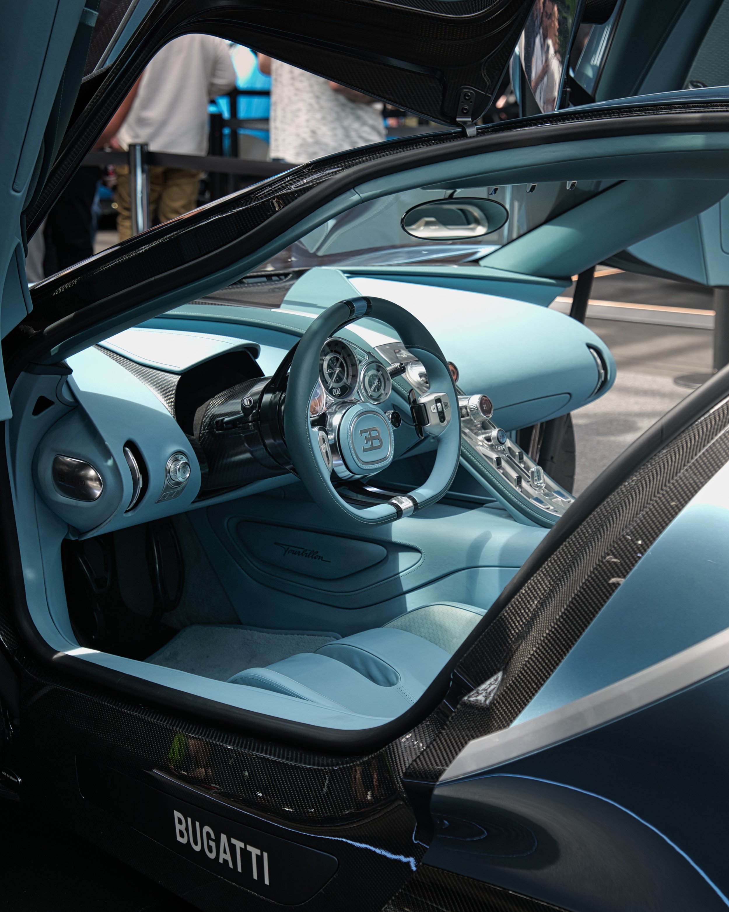 Intérieur d'une voiture de luxe Bugatti, mettant en avant le tableau de bord et le volant dans un design moderne et sophistiqué, avec des matériaux de haute qualité en bleu clair et éléments en carbone visible.