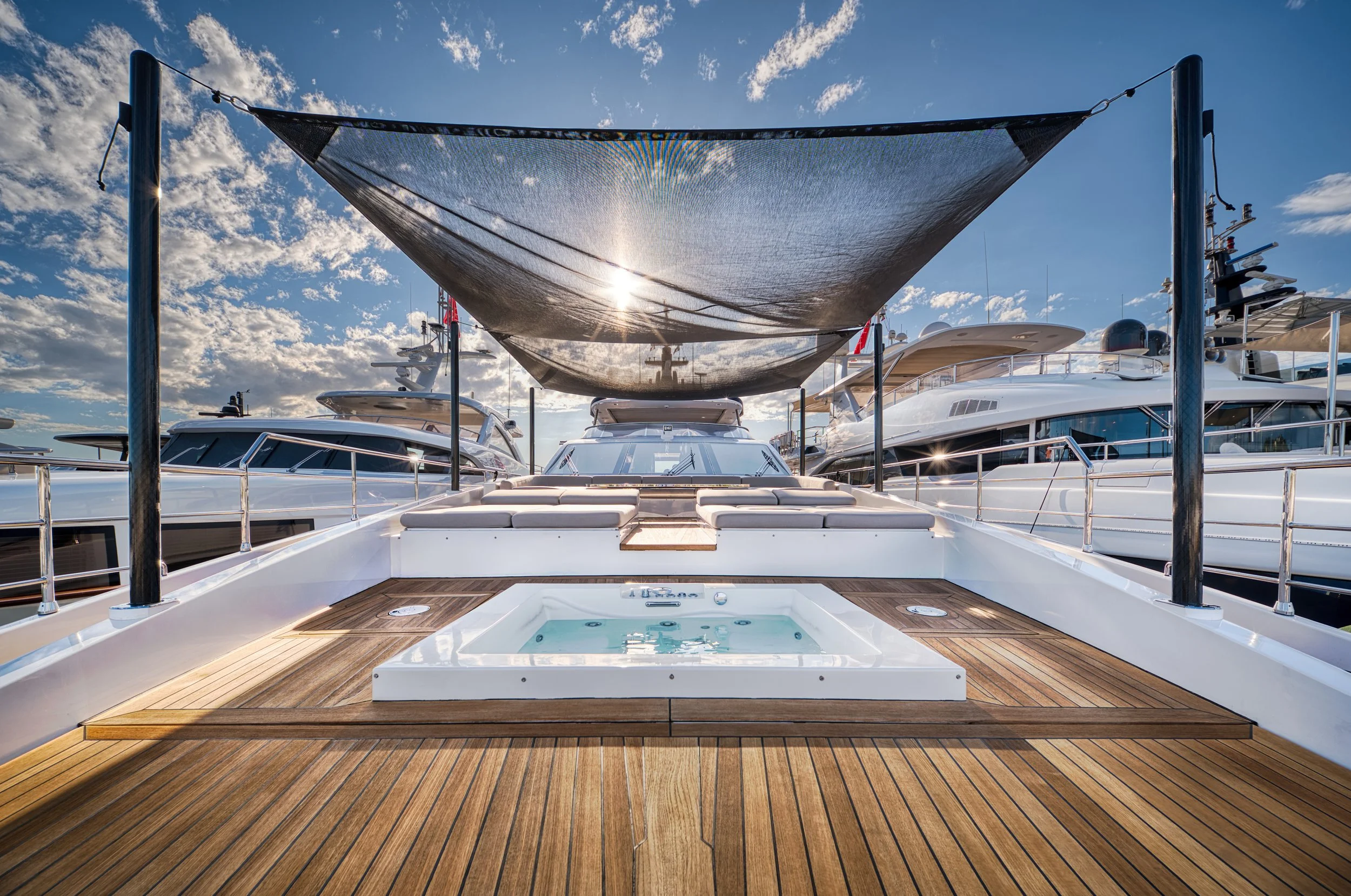 Une photo d'un yacht de luxe avec une plateforme en bois, une piscine, et un écran d'ombrage, sous un ciel bleu avec quelques nuages.