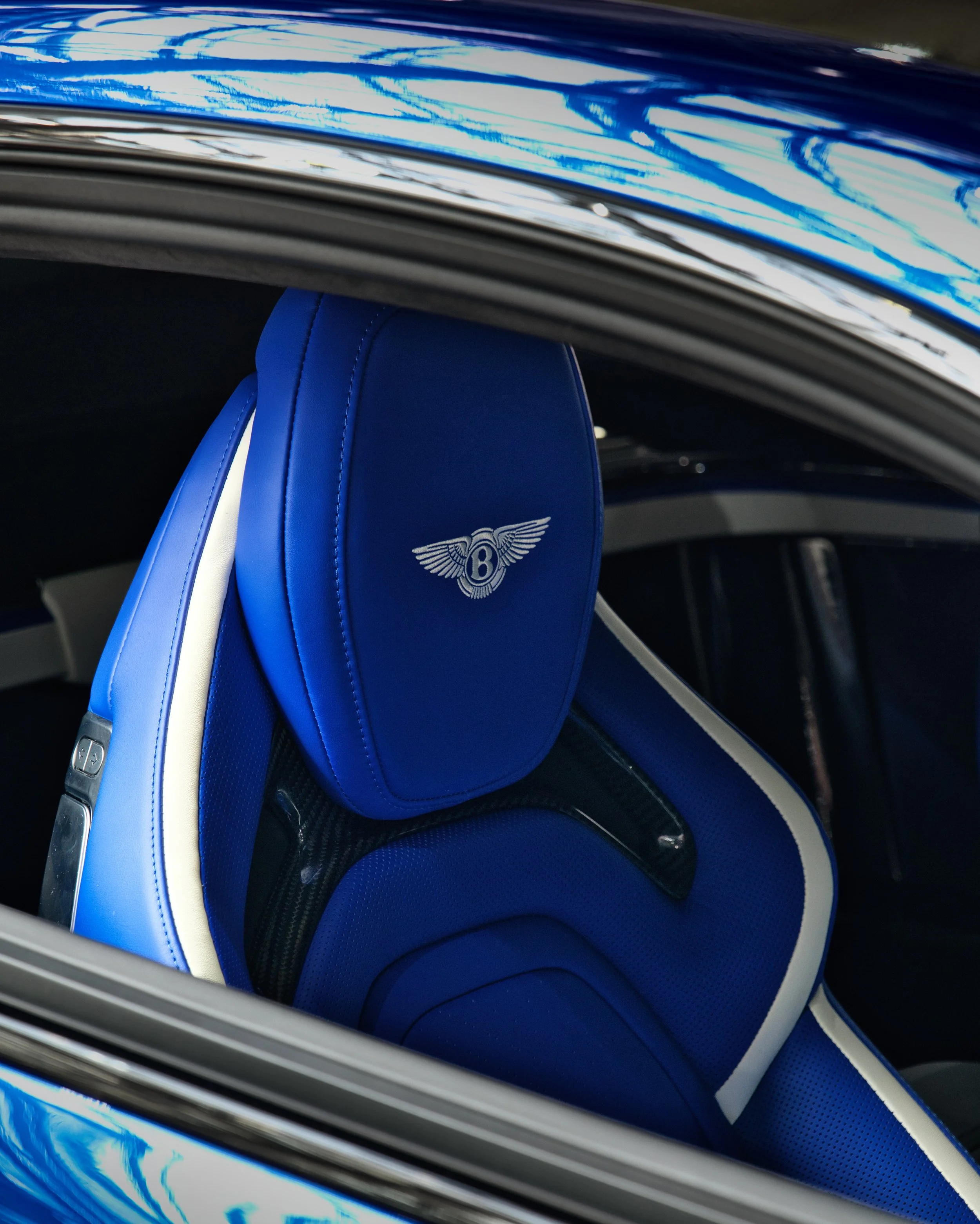 Intérieur d'une voiture de luxe avec des sièges en cuir bleu, portant un logo Bentley.