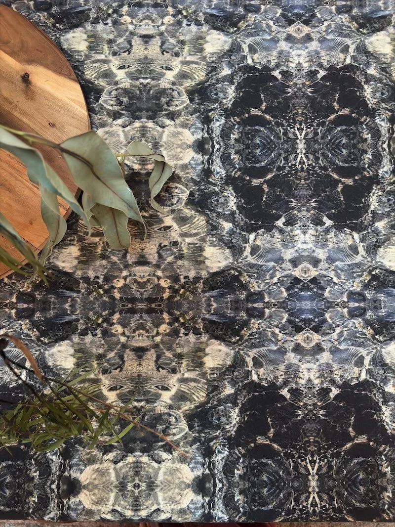 Blue Diamond fabric pattern of tidal water in an organic abstract repeat, printed on cotton linen styled with native foliage on a timber surface.