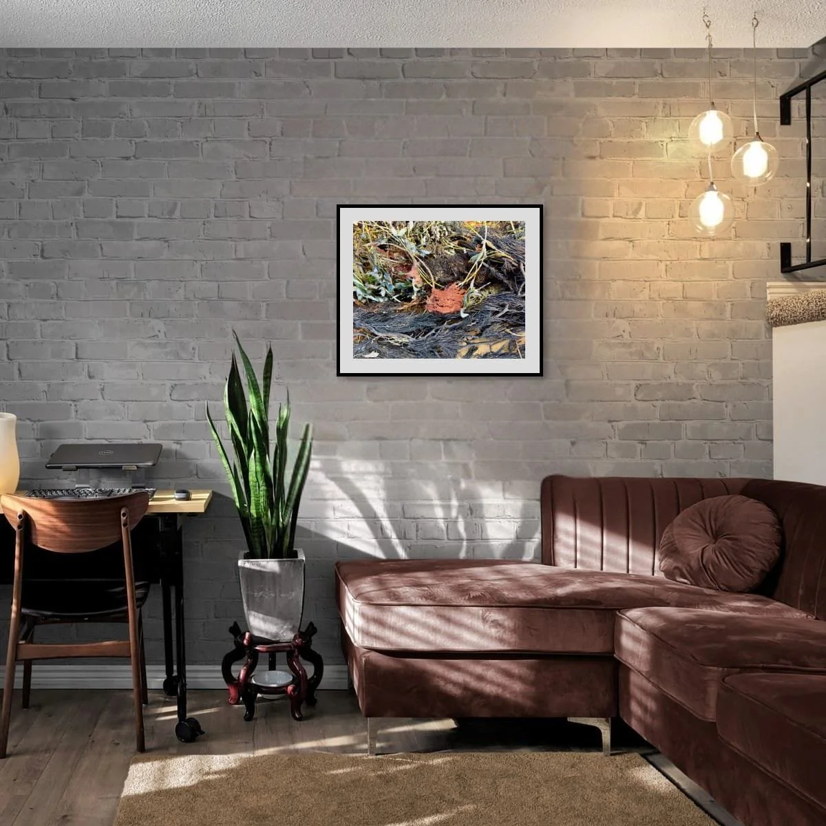 Framed print of Intertidal on a whitewashed brick wall above a maroon velvet sectional sofa. The black frame and the rust tones in the photograph echo the warm maroon of the couch.