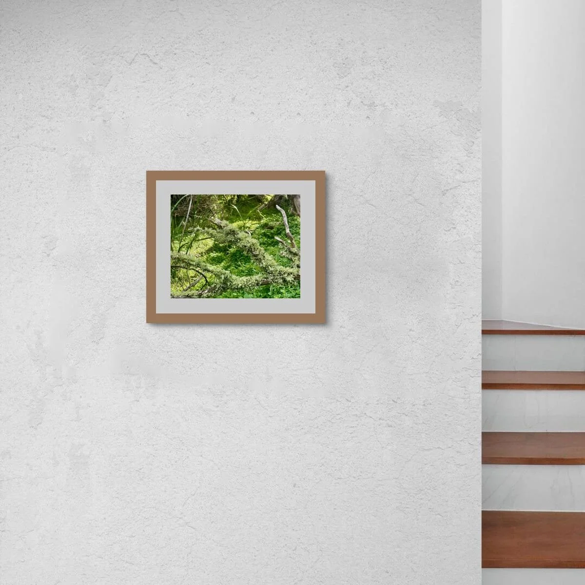 Framed print of Lichen Threads on textured white render beside a timber staircase. Warm timber frame echoes the stair treads. Vivid greens stand out against the pale wall.