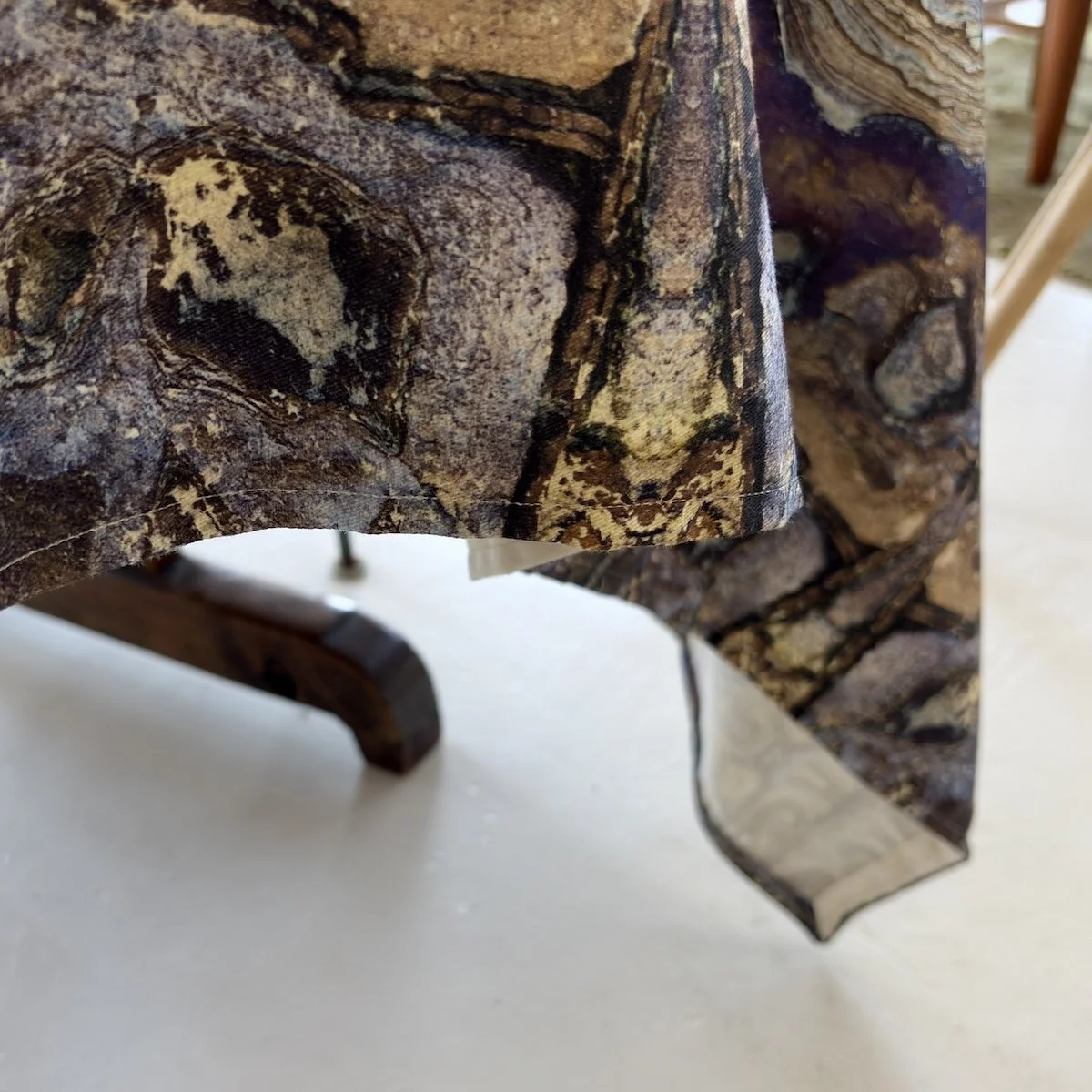 Close-up of a tablecloth and hem with a detailed natural print of an organic abstract rock, featuring shapes and patterns in shades of mauve, blues and sand.