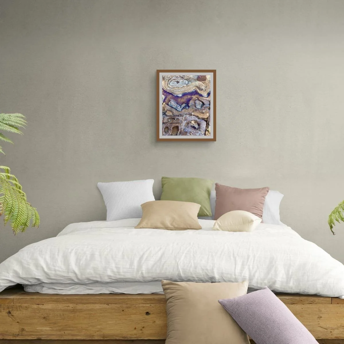 Bedroom mockup with a framed abstract print above a low bed against a soft grey green wall, styled with white bedding, pastel cushions and plants