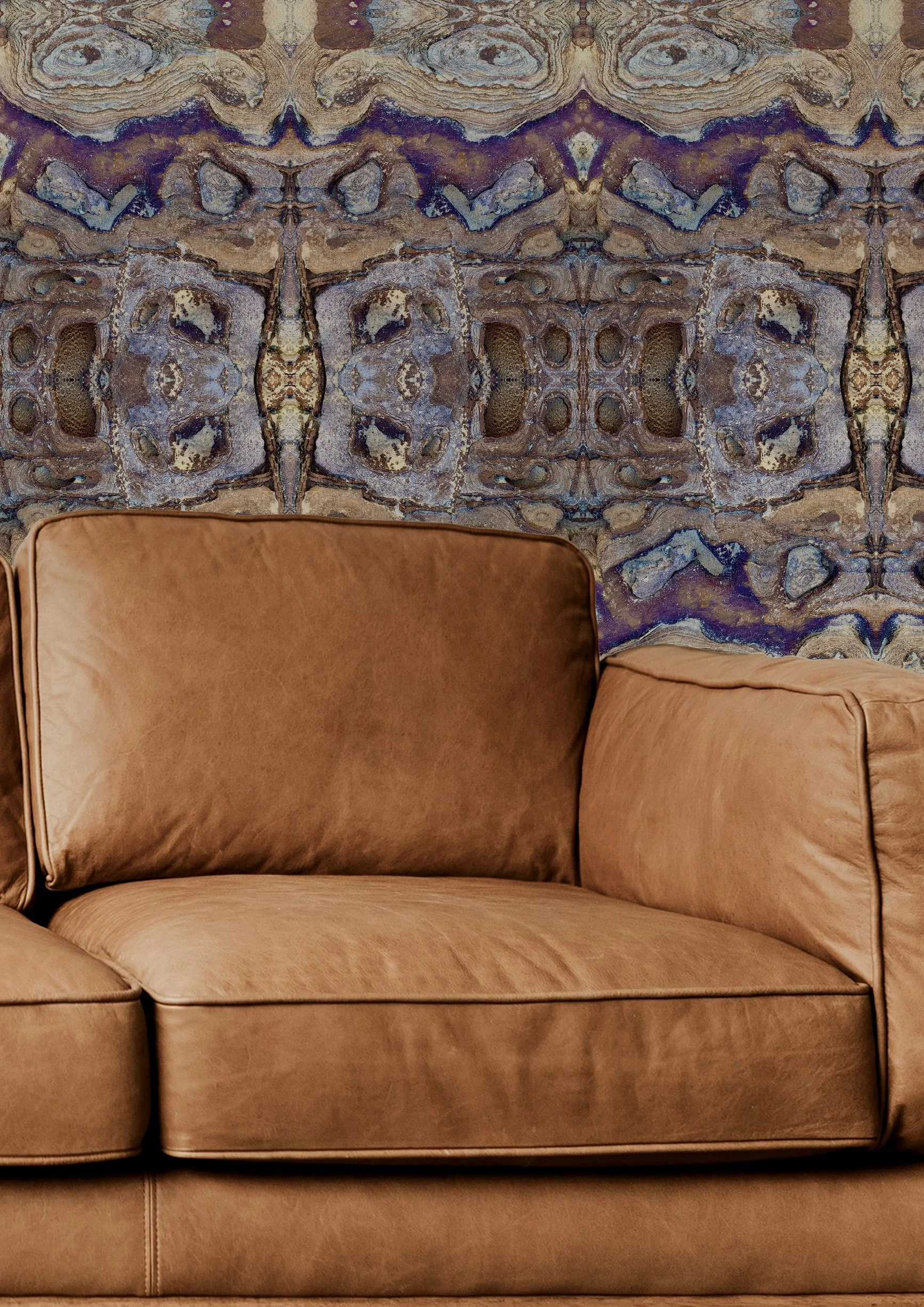 A nature-inspired and symmetrical patterned wallpaper, featuring images of birds and branches, creating a kaleidoscopic effect. In front there is a small white table with a stack of books and a potted plant with dark green leaves.