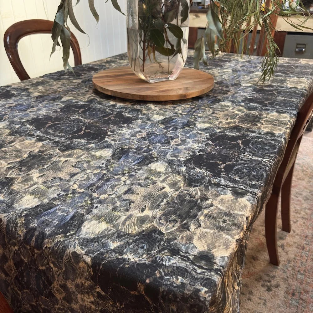 Blue Diamond tablecloth on a dining table with timber chairs, styled with eucalyptus foliage in a glass vase on a timber board.