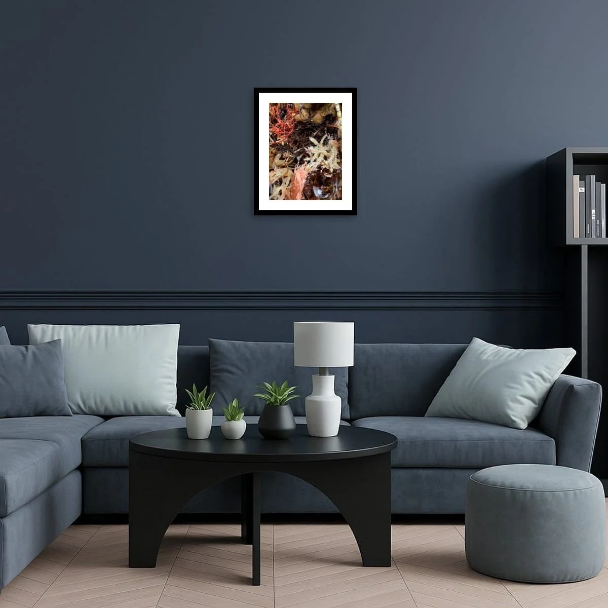 Framed seaweed artwork displayed on a deep blue wall above a sofa, the organic reds and creams contrasting with the calm, modern interior.