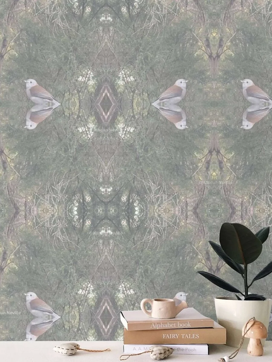 A nature-inspired and symmetrical patterned wallpaper, featuring images of birds and branches, creating a kaleidoscopic effect. In front there is a small white table with a stack of books and a potted plant with dark green leaves.