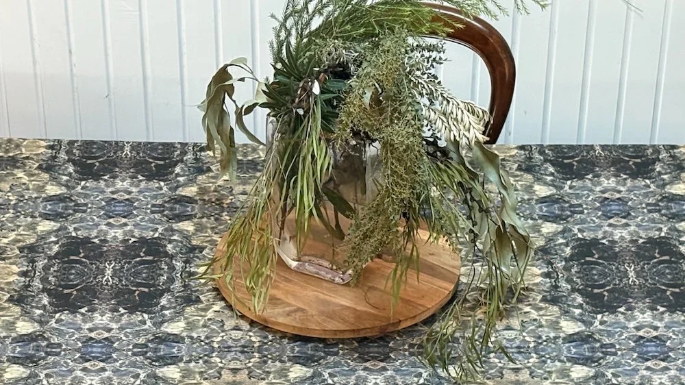 Blue Diamond tablecloth on a dining table styled with cascading native foliage arrangement on a timber board.