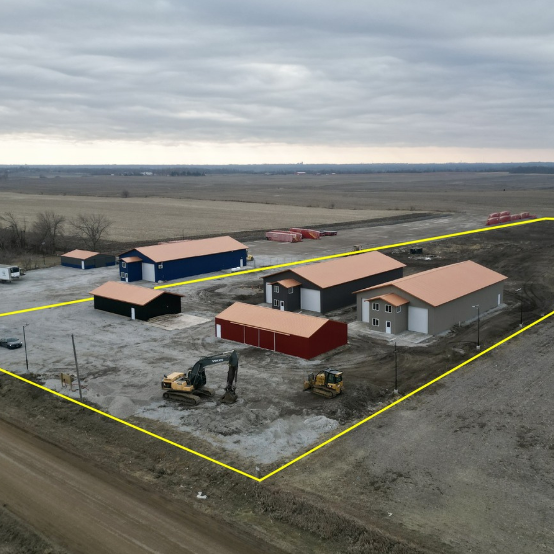 Construction site with several new houses being built in a rural area, surrounded by fields and overcast sky.