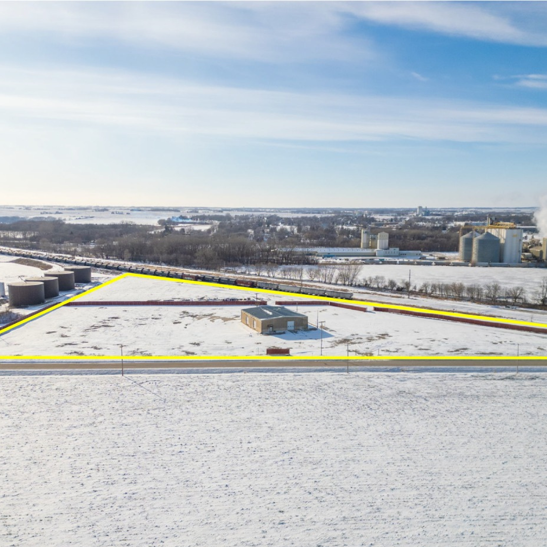 Snow-covered rooftop and industrial area in the distance with power lines and trees under a cloudy sky.