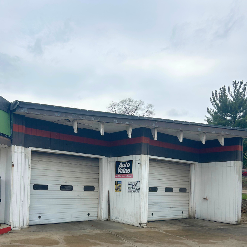 An auto repair shop with two closed garage doors, a sign that reads 'Auto Value,' and a cloudy sky overhead.
