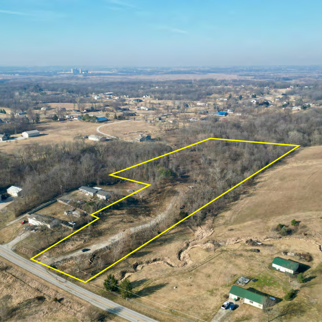 Aerial view of a large rural property outlined in yellow, with trees, open fields, and some buildings, under a partly cloudy sky.