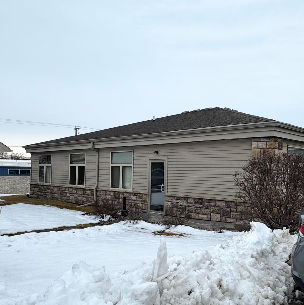 Side view of a house with beige siding, stone foundation, and snow-covered yard.