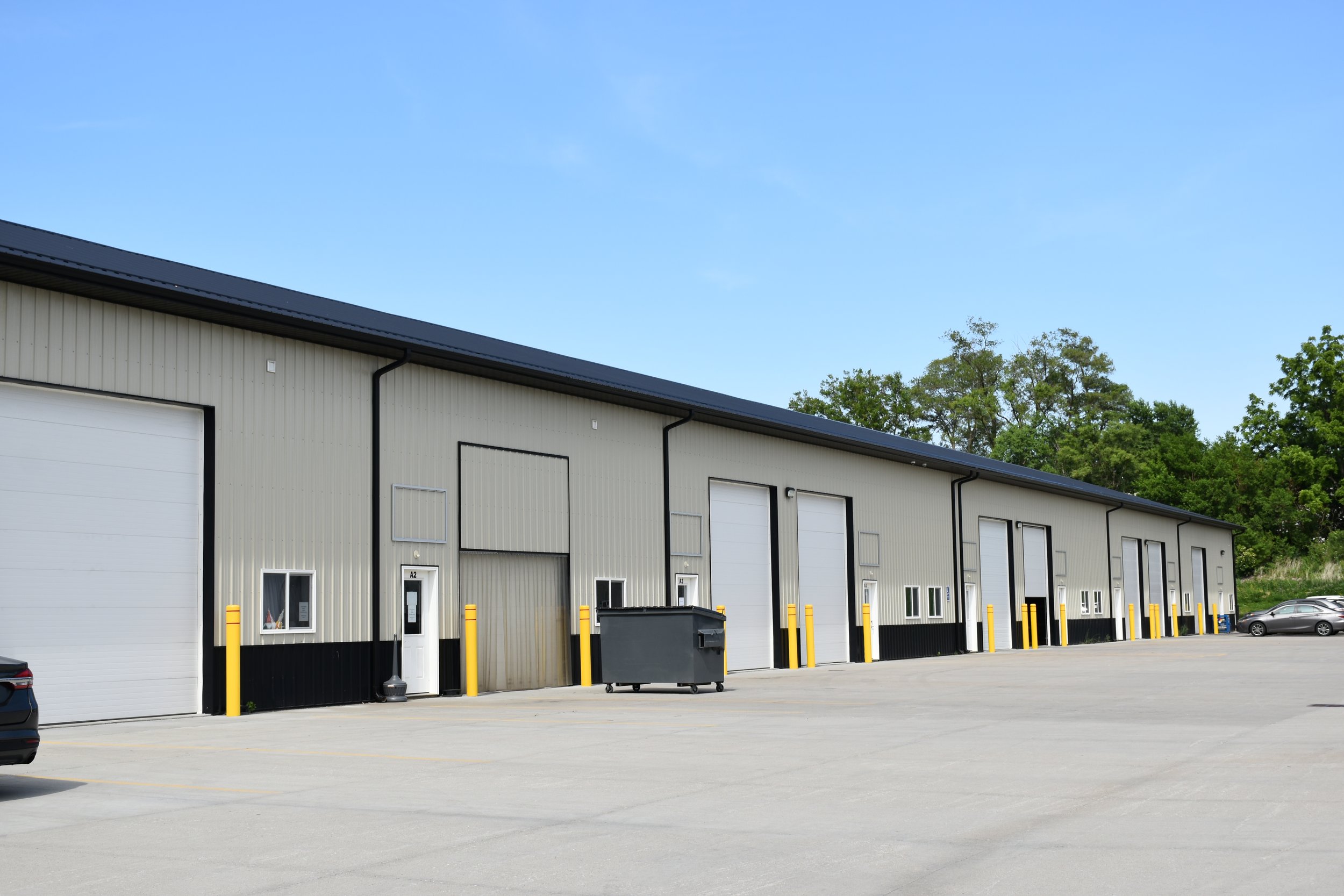 Large industrial warehouse with multiple garage doors, parked trucks, and clear blue sky with bright sunlight.