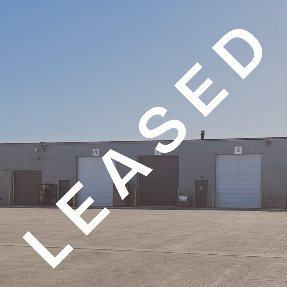 Large industrial warehouse with five loading dock doors numbered 4, 3, 2, 1, and an additional unnumbered door, situated in an expansive parking lot on a clear, sunny day.