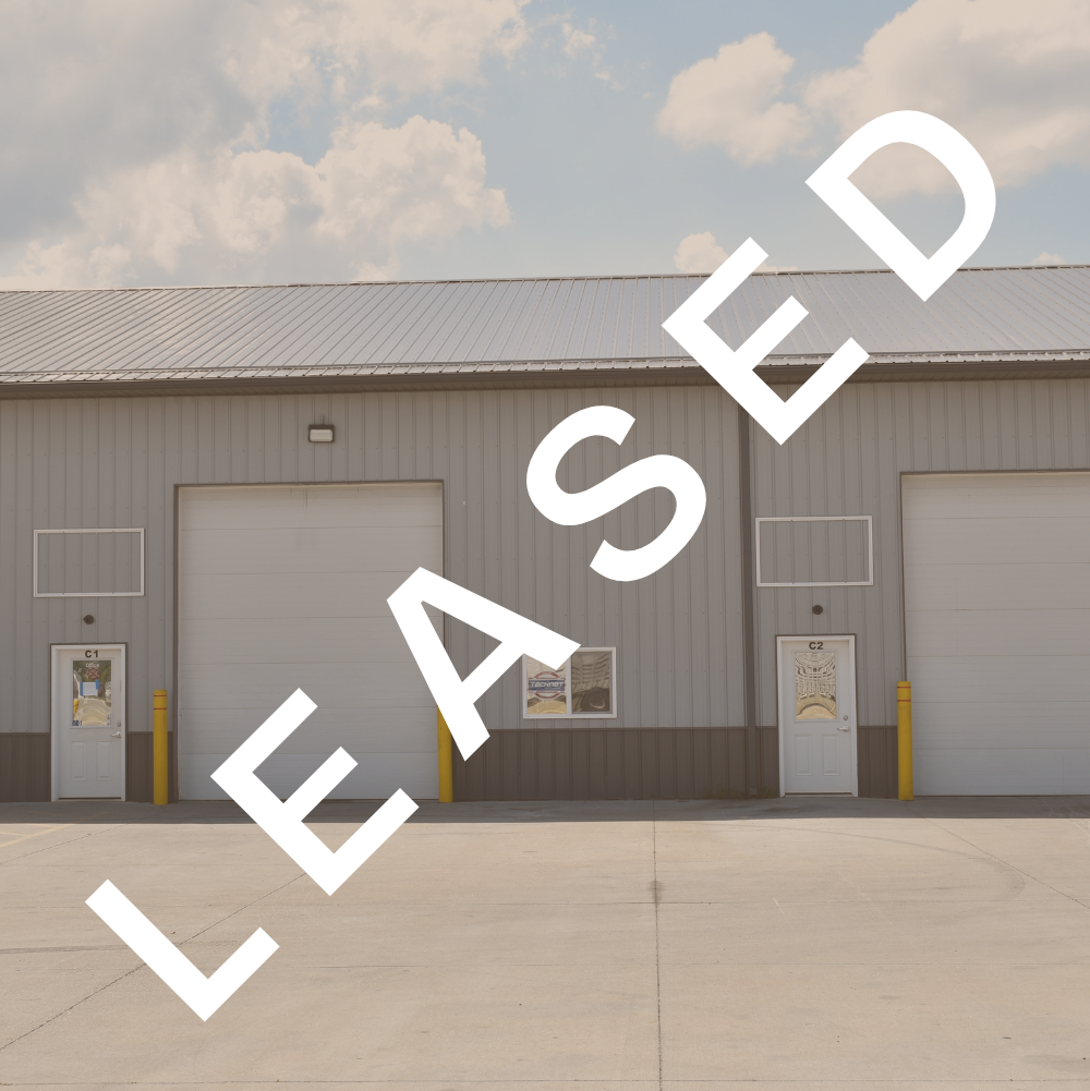 Large industrial building with multiple loading docks, parking lot in front, and clear blue sky. Sections labeled 'Suites C1-C4' and 'Suite C5'.