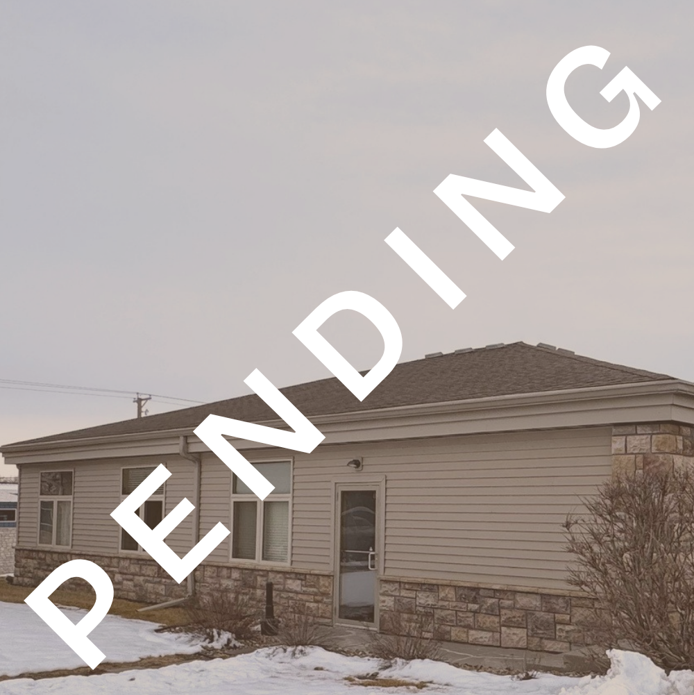 Side view of a house with beige siding, stone foundation, and snow-covered yard.