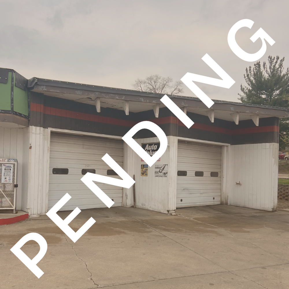An auto repair shop with two closed garage doors, a sign that reads 'Auto Value,' and a cloudy sky overhead.