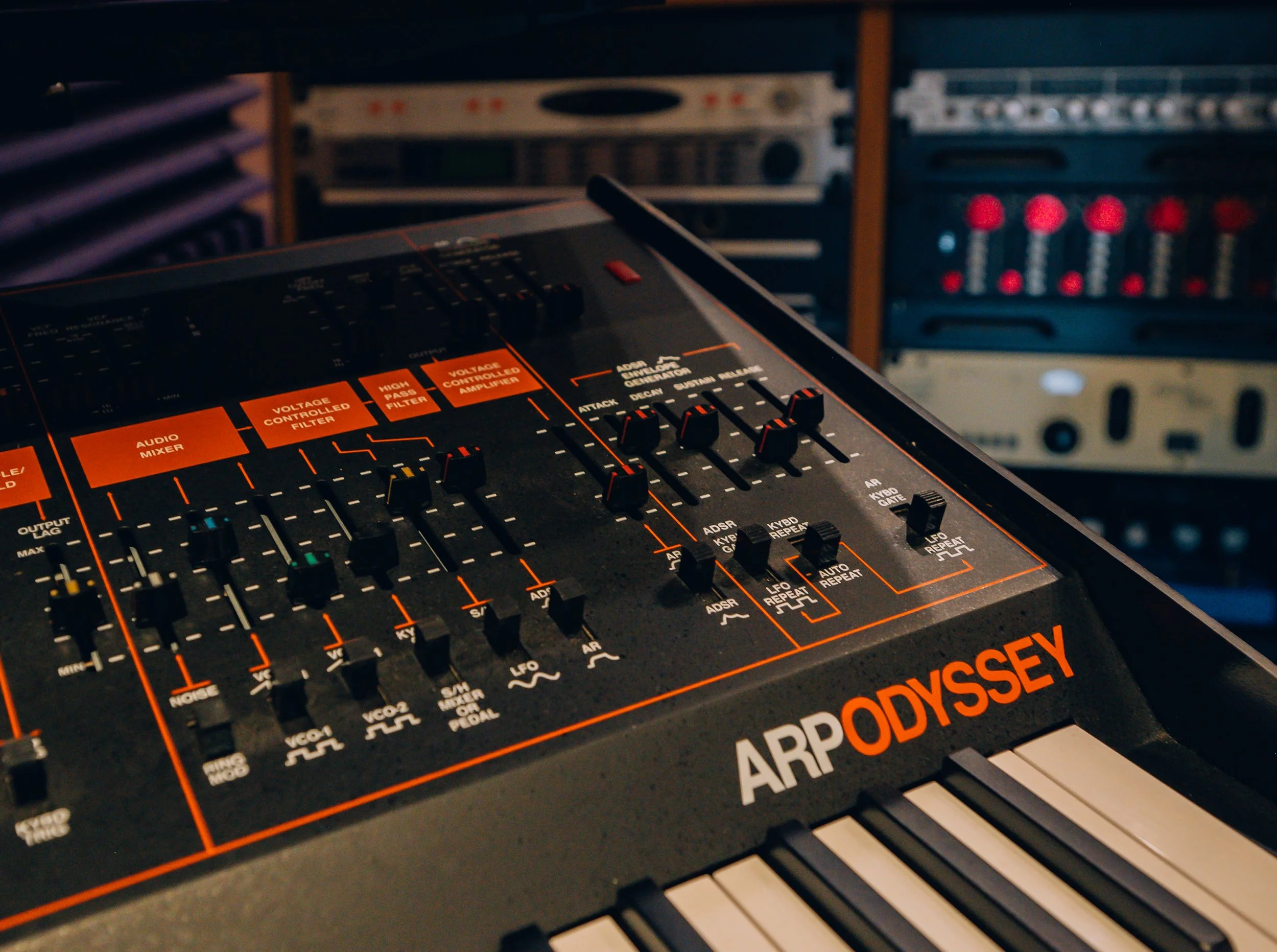 Close-up of a vintage ARP Odyssey synthesizer with sliders, knobs, and labels in a music studio.