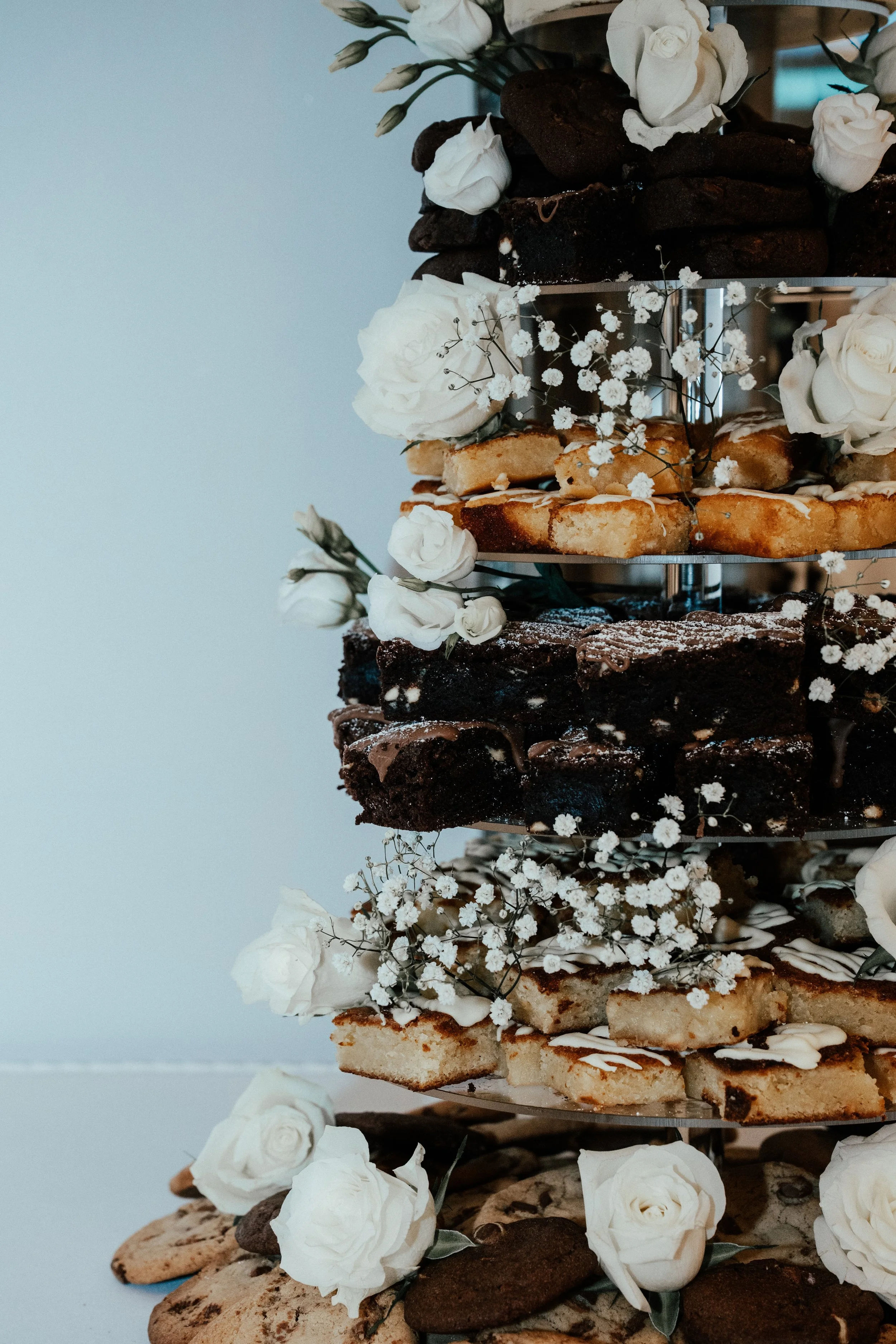 Tiered dessert stand with cookies, blondies, and brownies decorated with white roses and baby's breath flowers.