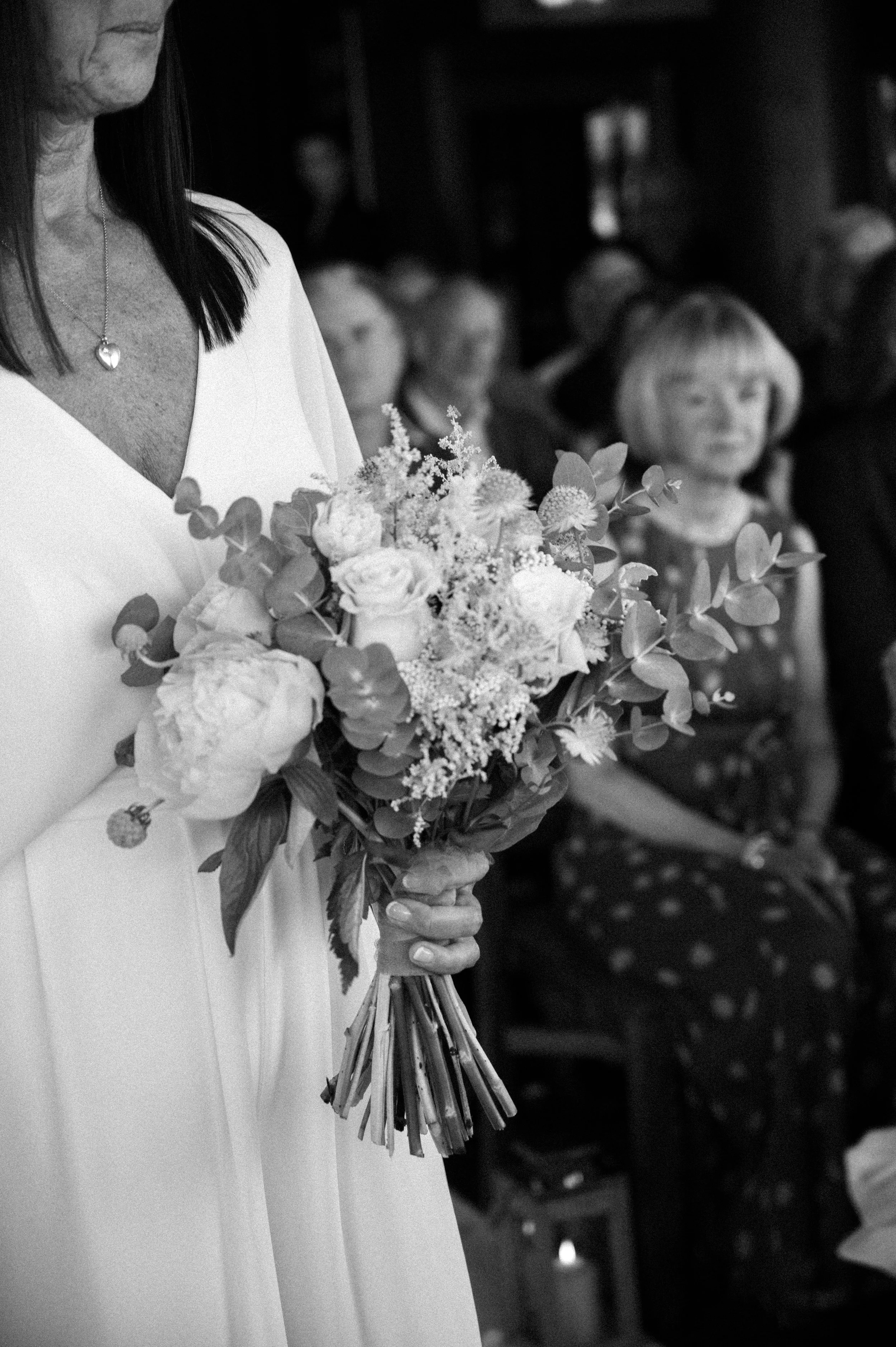 A woman holding a bouquet of flowers during a ceremony, with seated people in the background.