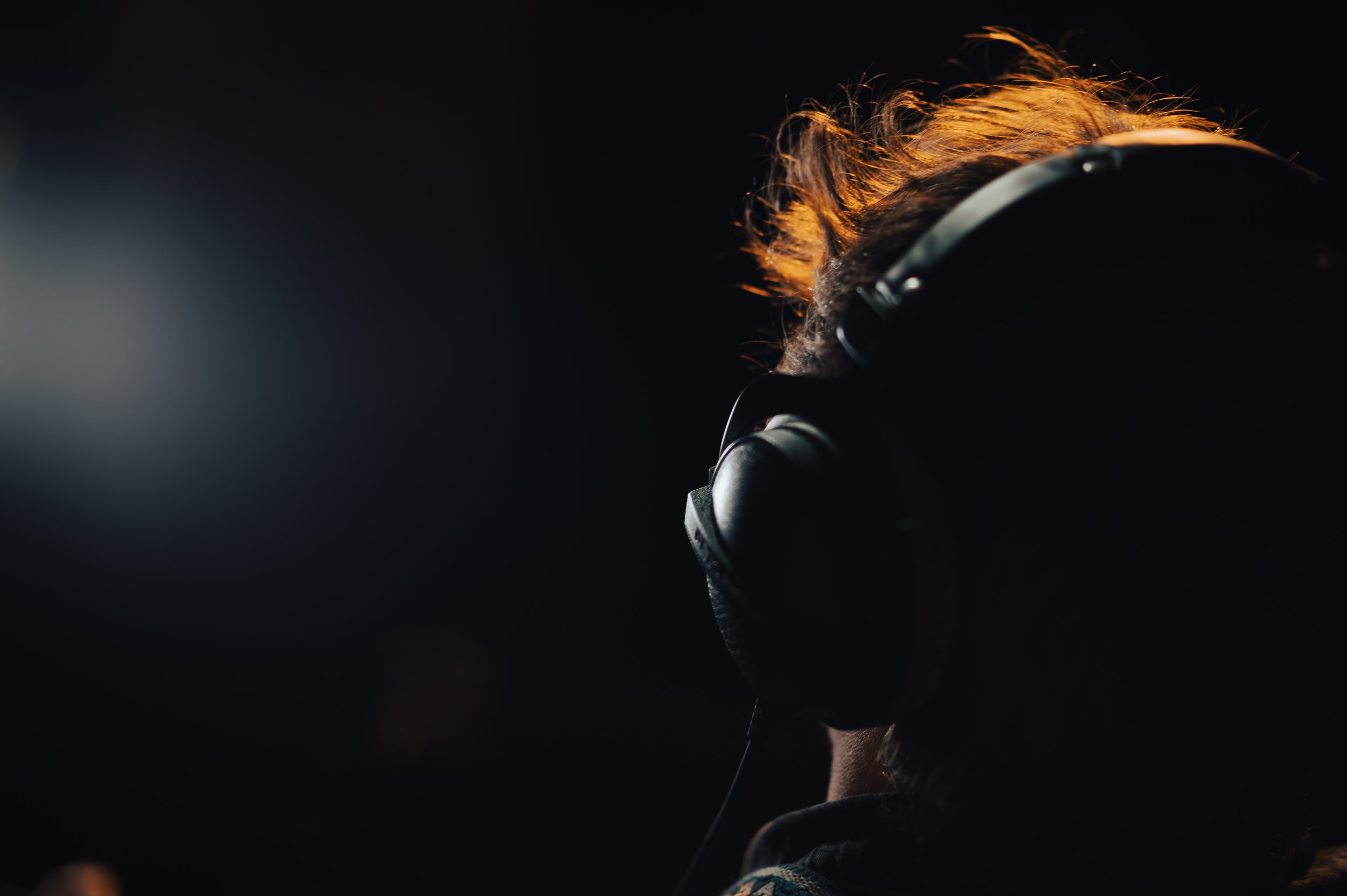 Person wearing large headphones with orange hair visible in a dark environment