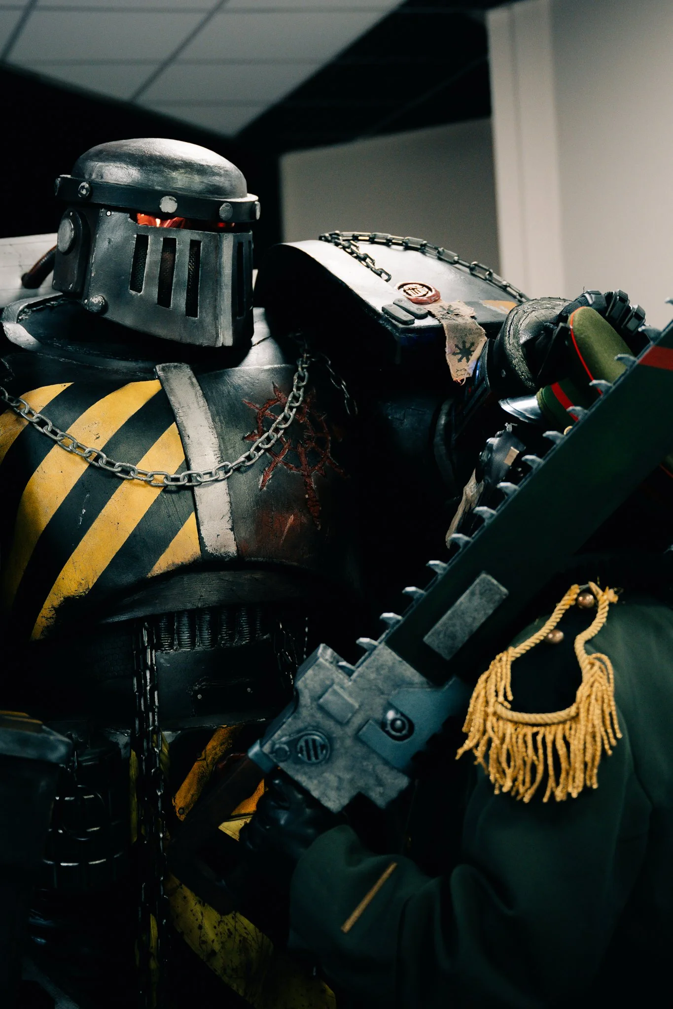 Close-up of a life-sized model of a futuristic armored soldier with a helmet, black armor with yellow stripes, chains, and holding a large gun.