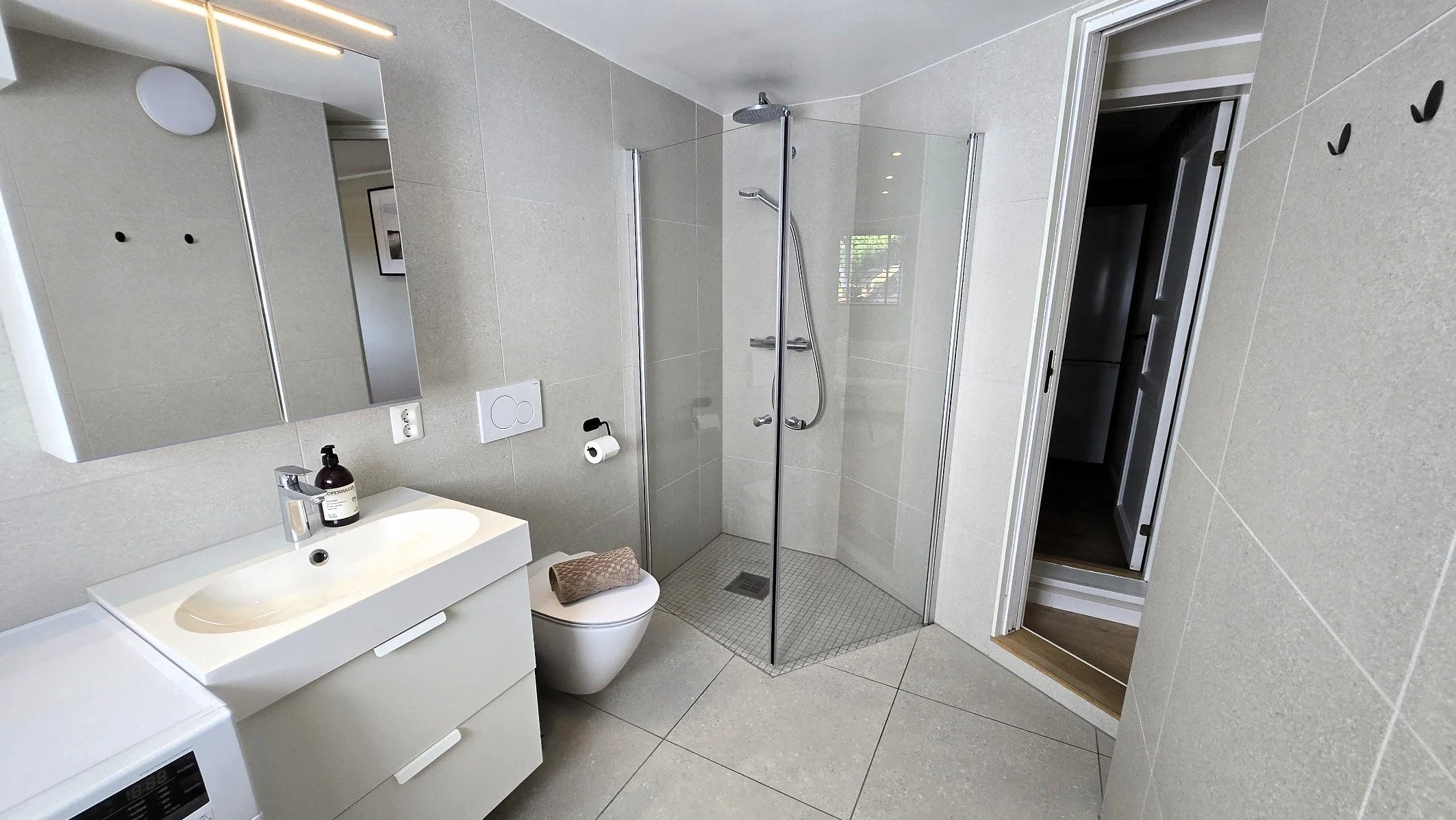 Modern bathroom with beige tiled walls and floor, glass shower enclosure with a rain shower head.